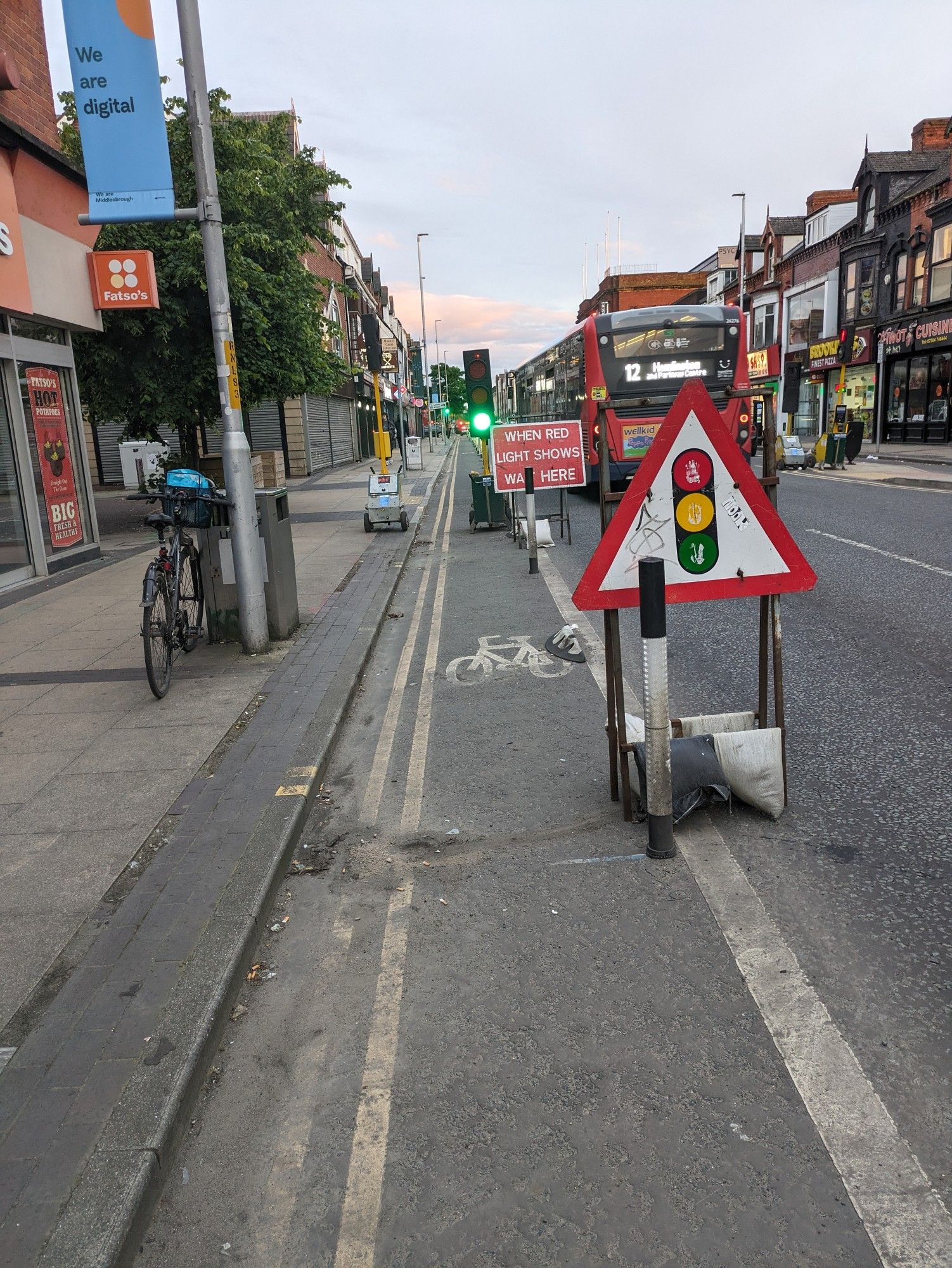 Same street, traffic light and red light warning sign moved to the boundary of the bike lane with the car lane, and stop light shifted enough that bikes can pass. My bike is leaning on a lamppost while I move the signs.