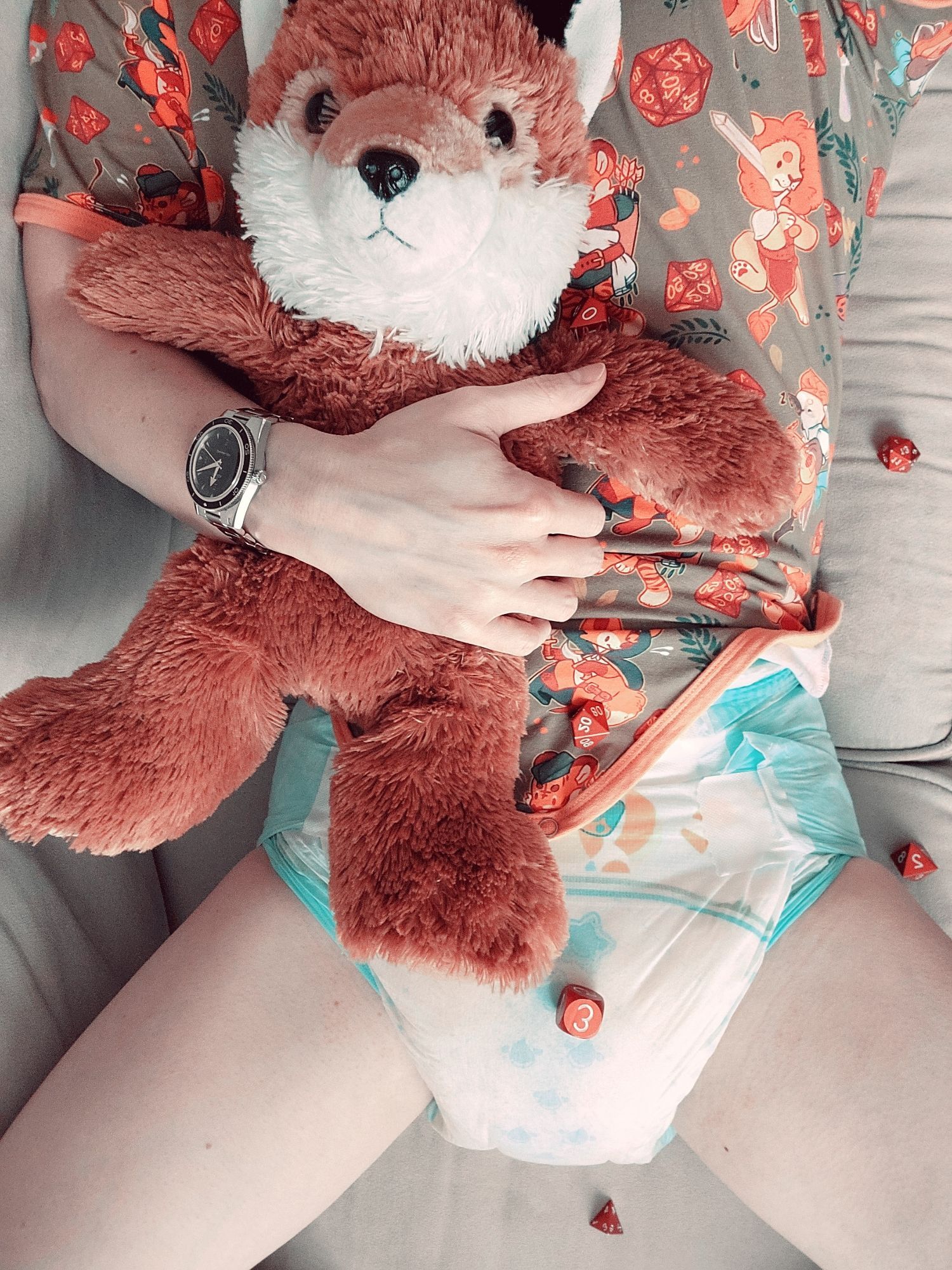 Me laying on the couch, snuggling my plush fox. I'm wearing a green and orange onesie with a D&D themed print. I have a very wet diaper under it. There are orange D&D dice scattered about.