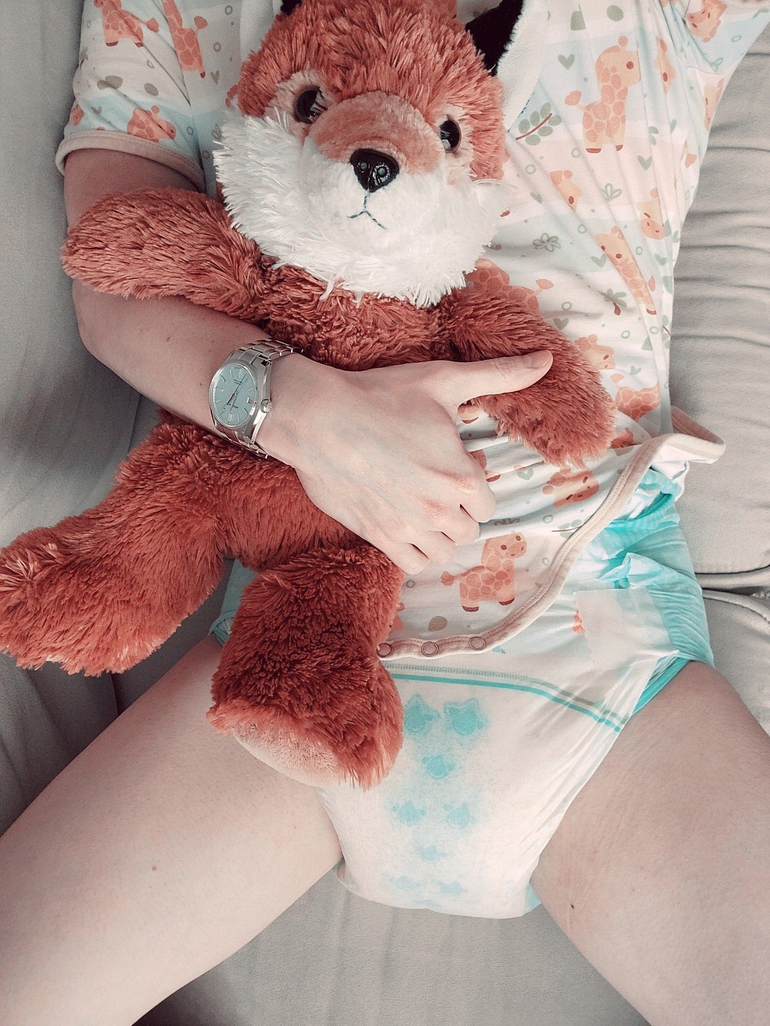 Me laying on the couch with my plush fox. I'm wearing a colorful giraffe themed onesie and a very wet diaper.