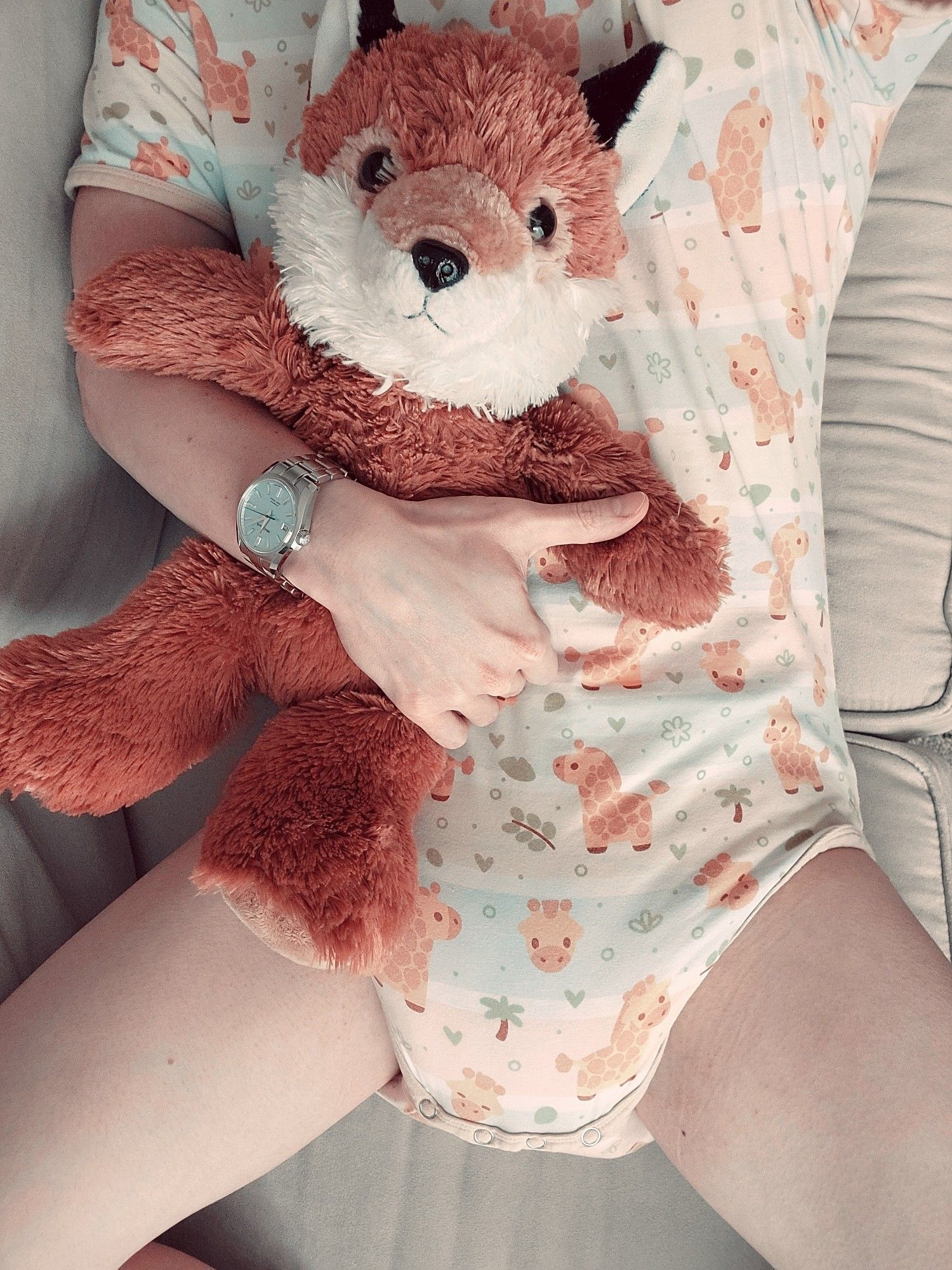 Me laying on the couch with my plush fox. I'm wearing a colorful giraffe themed onesie and a very wet diaper.