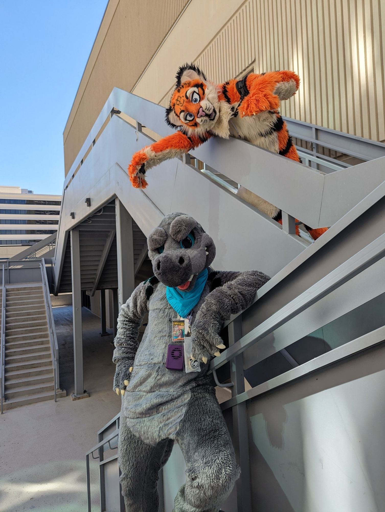 Nullstrukt the Dimetrodon fursuit and Zedd the tiger fursuit standing on two parts of a stairway outside. Nullstrukt is on the lower stairs, leaning against the railing and looking smug, unaware that he is about to be bapped by Zedd who is reaching down from the upper staircase.