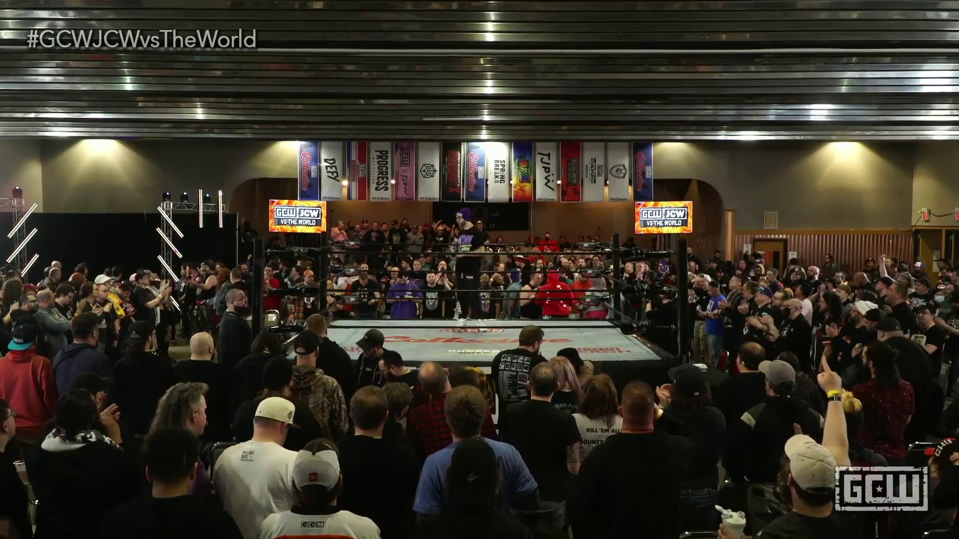 The image of a Game Changer Wrestling show. A wrestling ring surrounded by fans. Ring announcer Emil Jay standing in the center.