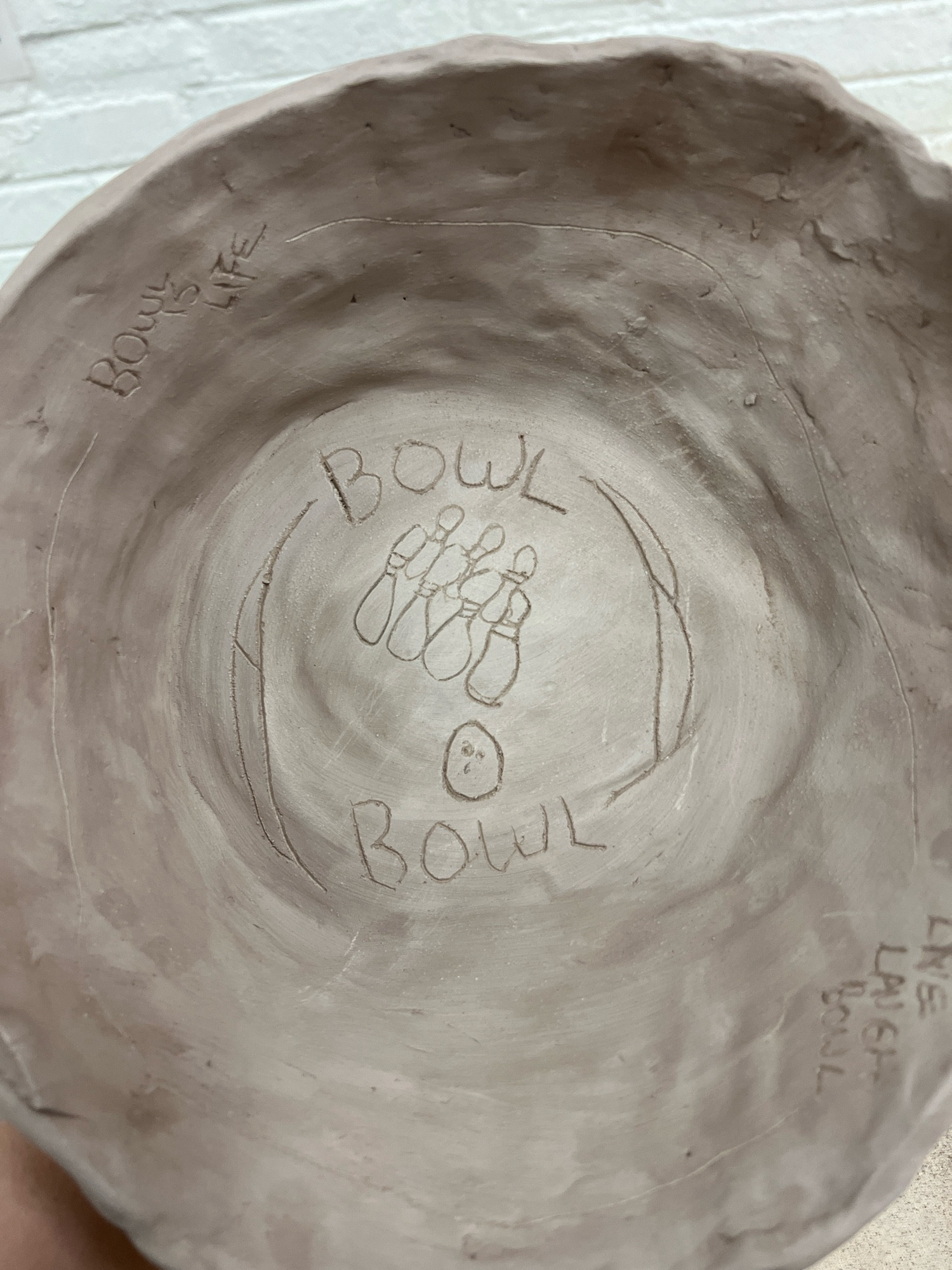 A clay bowl with “bowl bowl” etched into it, there are also bowling pins and a bowling ball etched in