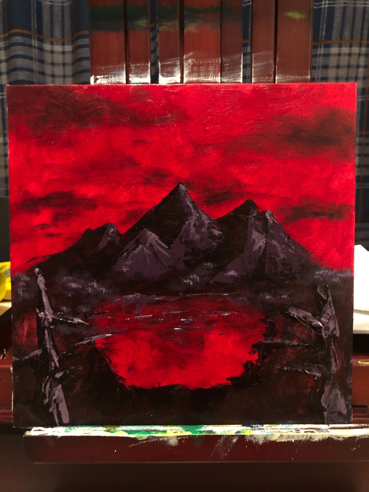 A painting of black mountains in the distance under a red sky, the lake is also red and it is flanked by two dead black trees