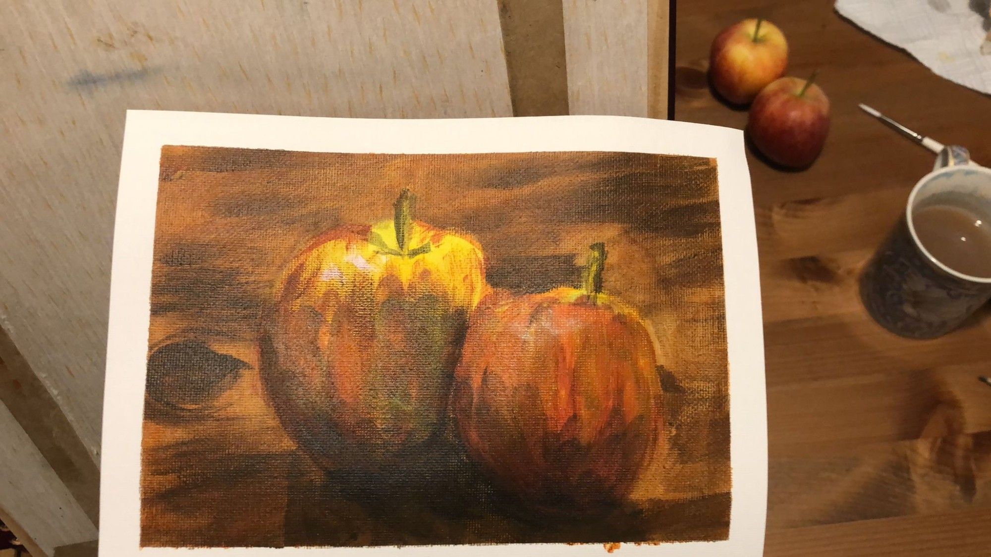 A painting of two apples on a wooden table