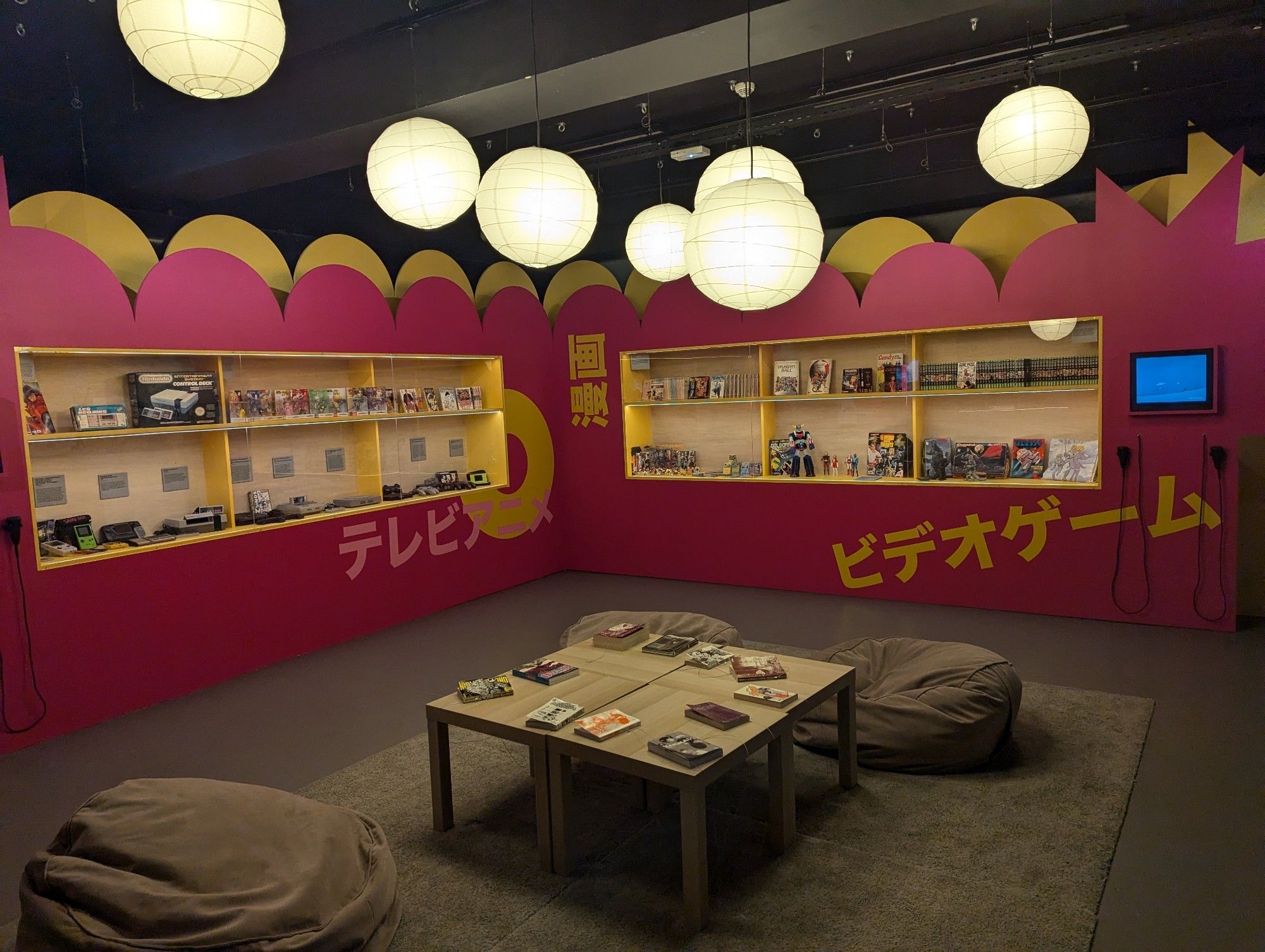 Une pièce avec une table des poufs et des mangas. Dans al vitrine des vieilles consoles et des figurines.