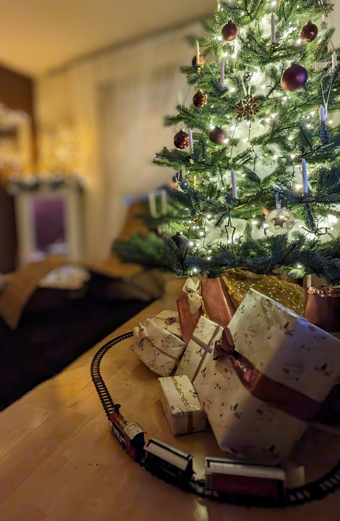 Man sieht einen Weihnachtsbaum, der in braun, gold und weiß geschmückt ist. Er steht auf einem Schlitten, unter ihm stehen Dekogeschenke und um alles Rum fährt eine Weihnachtseisenbahn