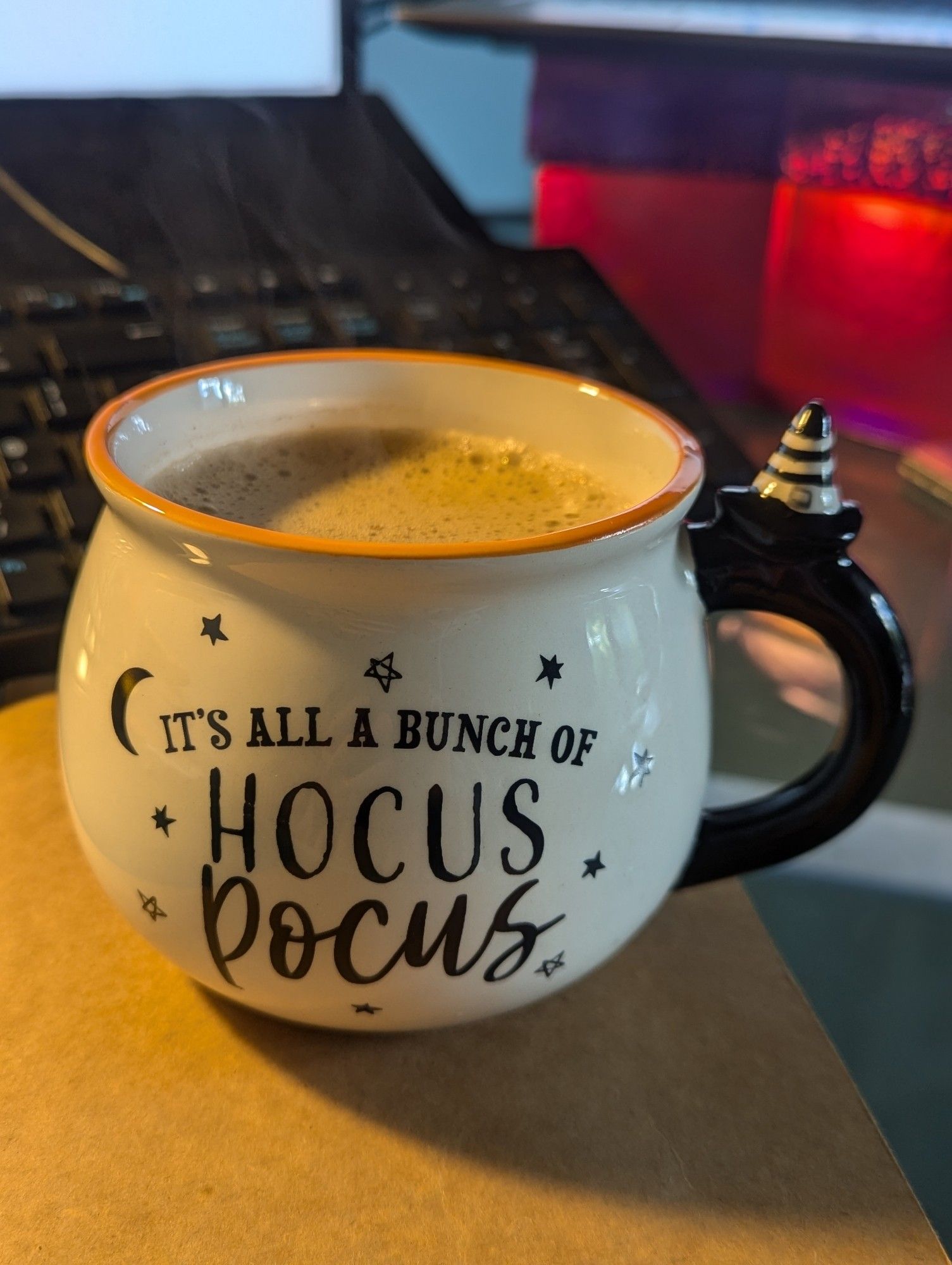 Halloween themed mug with the words It's all a bunch of hocus pocus. The mug is shaped Ike a cauldron and is white with an orange rim and a black handle with a black and white striped witch's hat perched at the top.