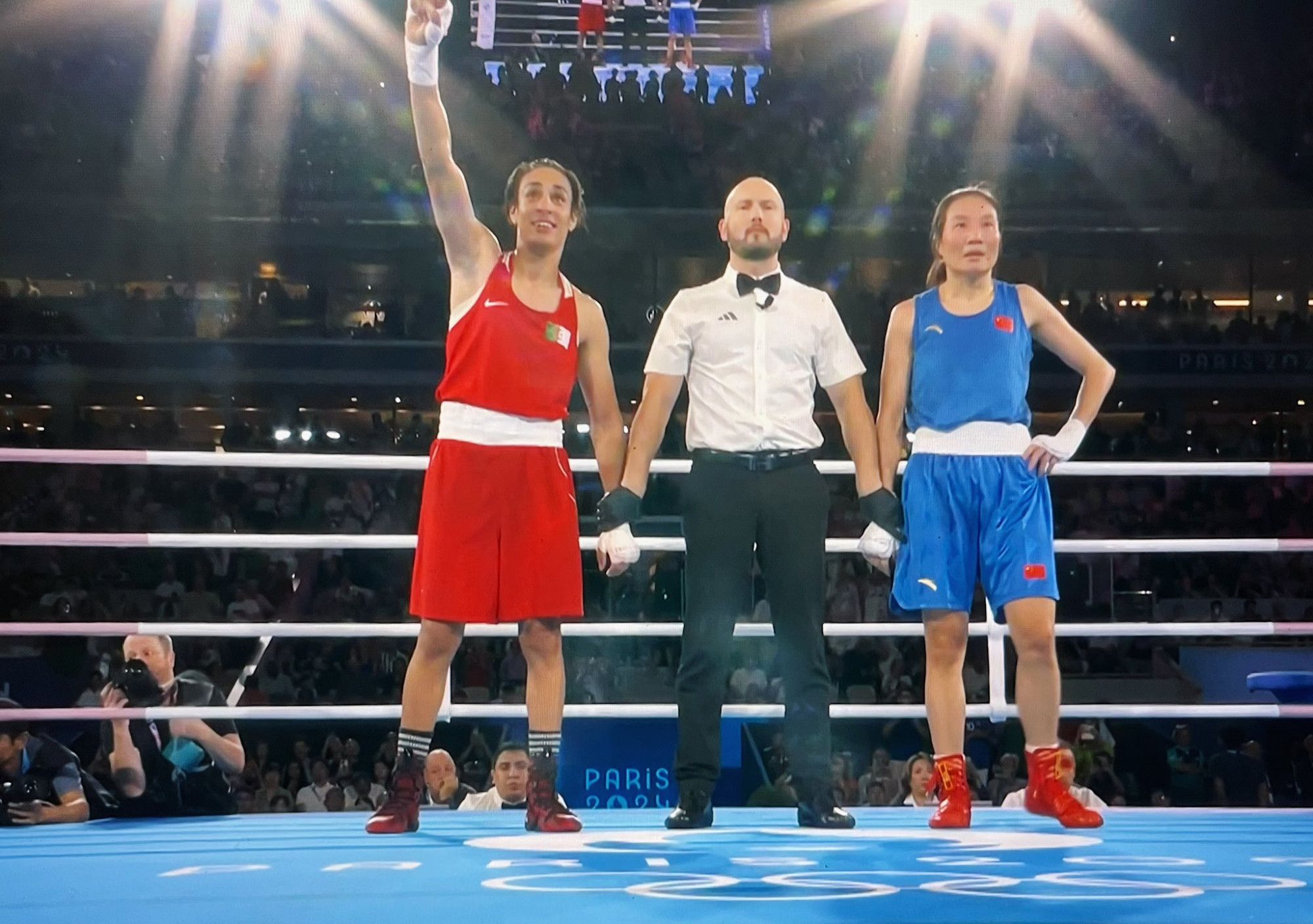 A picture of Imane Khelif, her opponent Yang Liu, and the referee of their gold medal fight, showing Imane Khelif the winner.