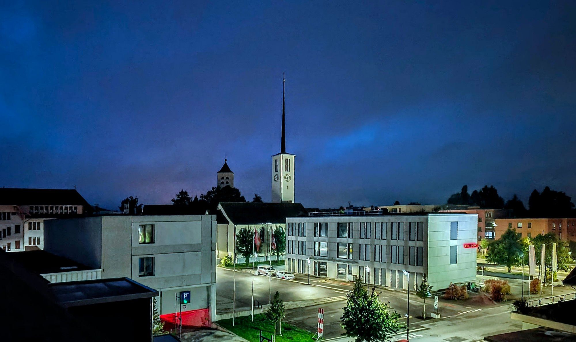 Bewölkt. Kirchen, Parkhaus und Bank, mittig leerer Platz.