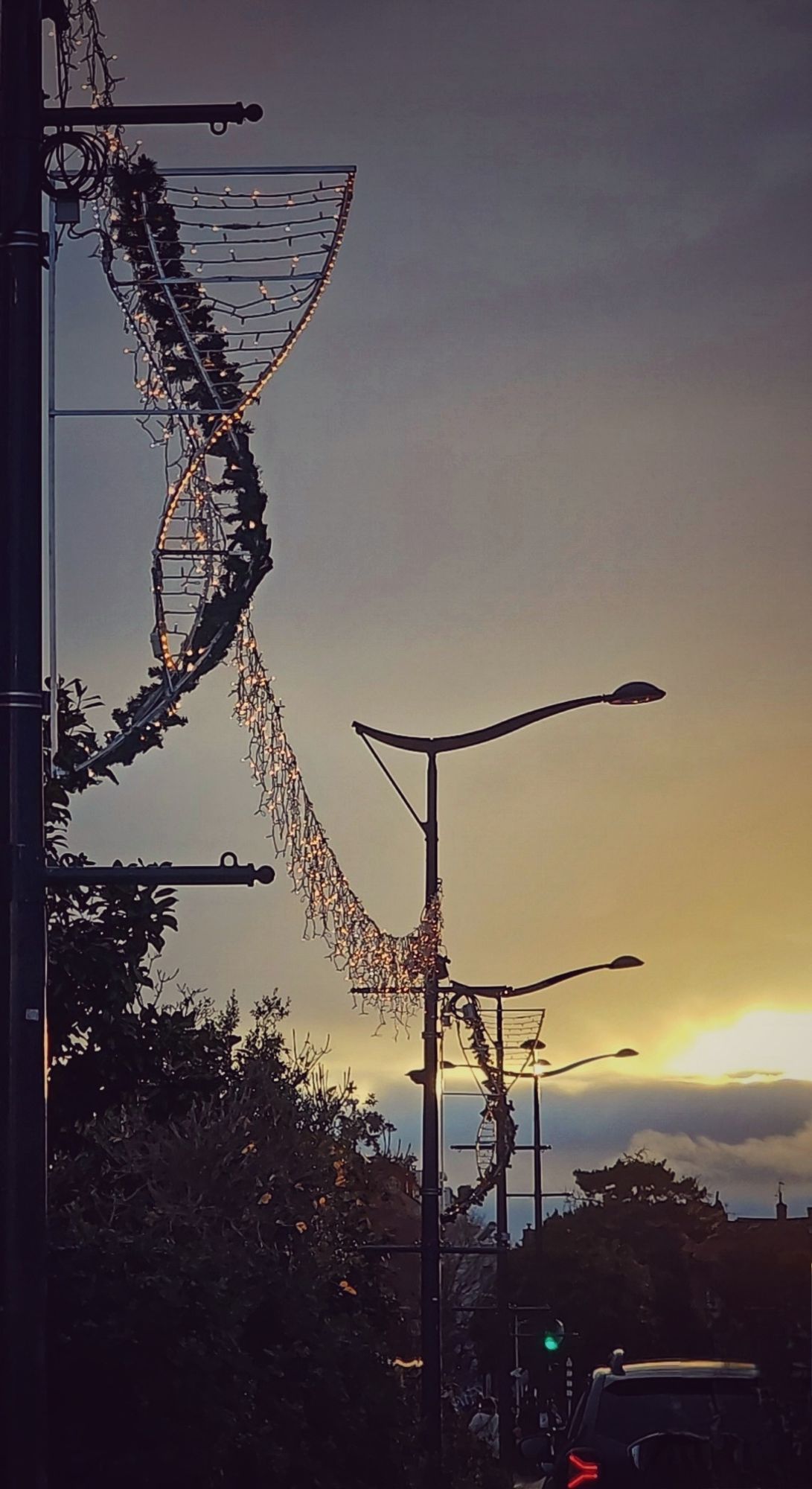 Lumières du soir.... le soleil se couche derrière les nuages, les lampadaires décorés avec les illuminations de Noël.