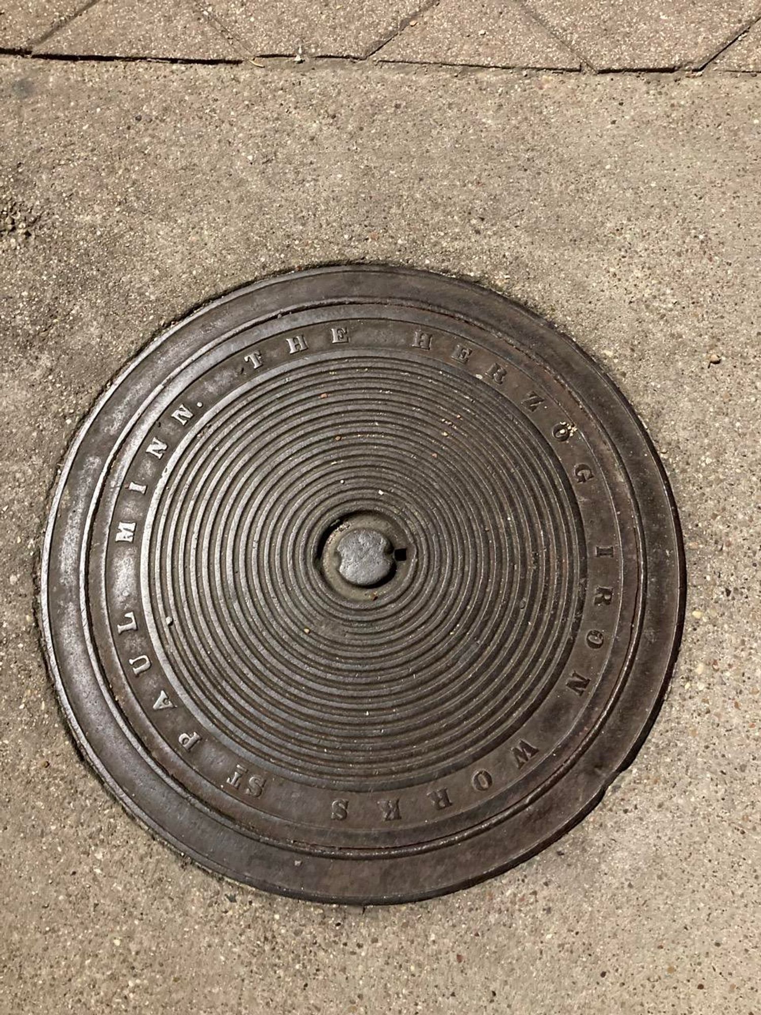 Round, old looking cover with a concentric circle design and the inscription „The Herzog Iron Works St. Paul Minn.“