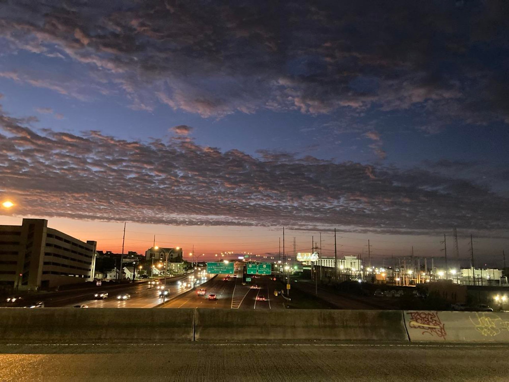 Blick von einer Brücke auf die darunter liegende Autobahn und einen Himmel mit Wolkenstreifen im Abendrot 