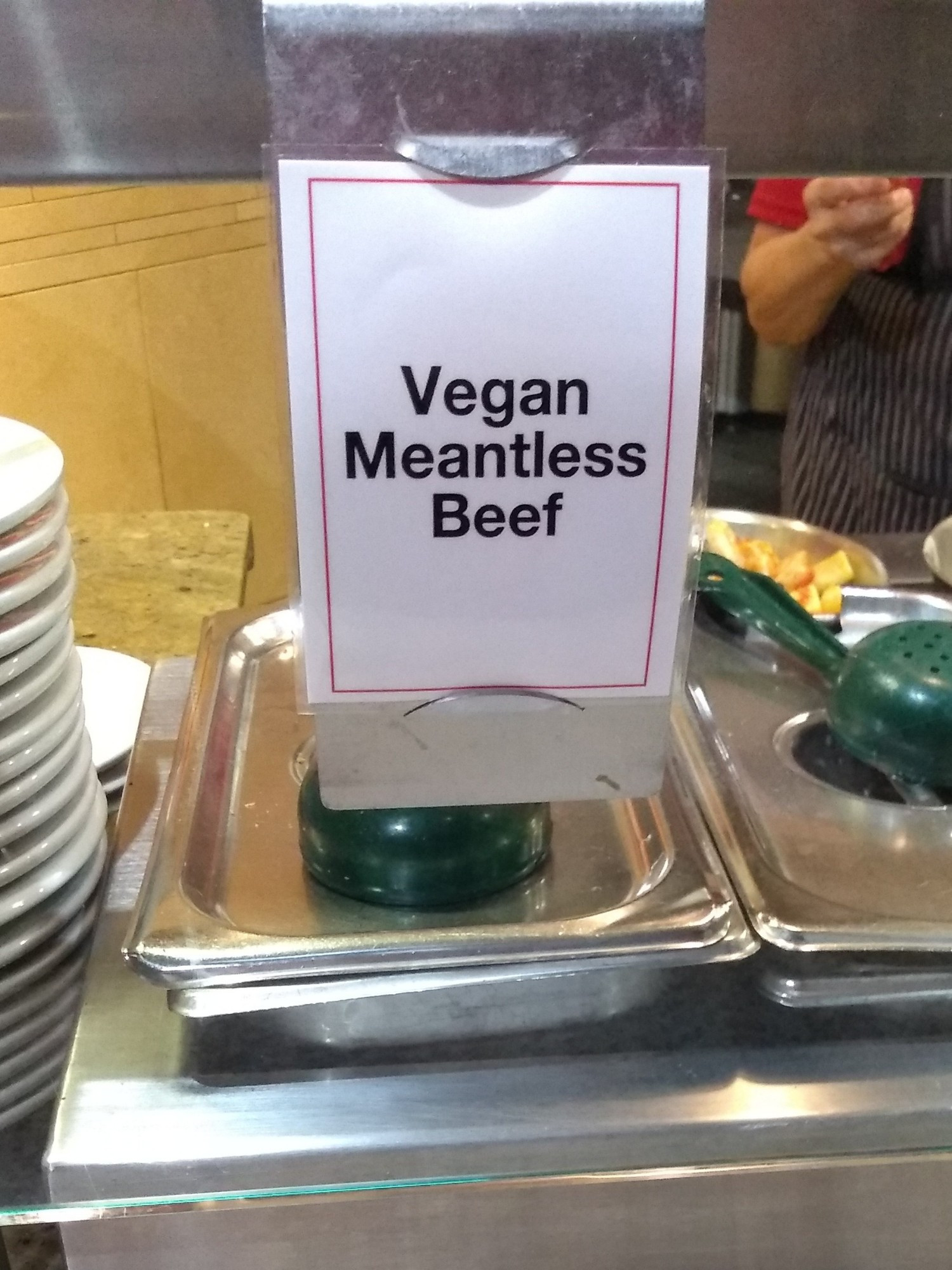 A sign over a sneeze guard that reads "Vegan Meantless Beef". Meatless with a N. Meantless.