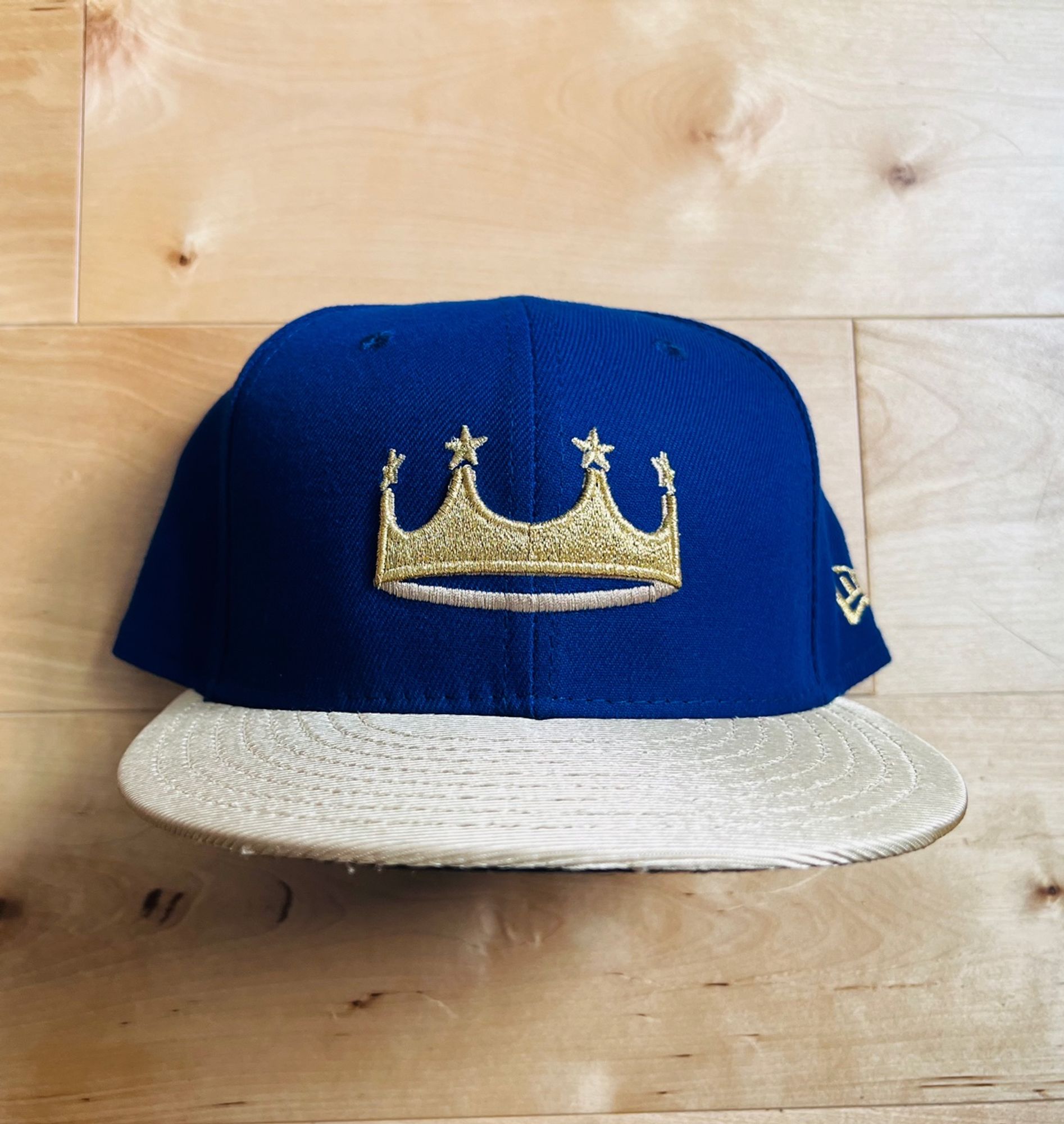 Kansas City Royals "Turn Ahead the Clock" hat from 2018. It features a blue crown with a metallic gold visor and button. On the blue crown is...a gold crown. The English language is full of mystery. The gold crown features four gold stars.