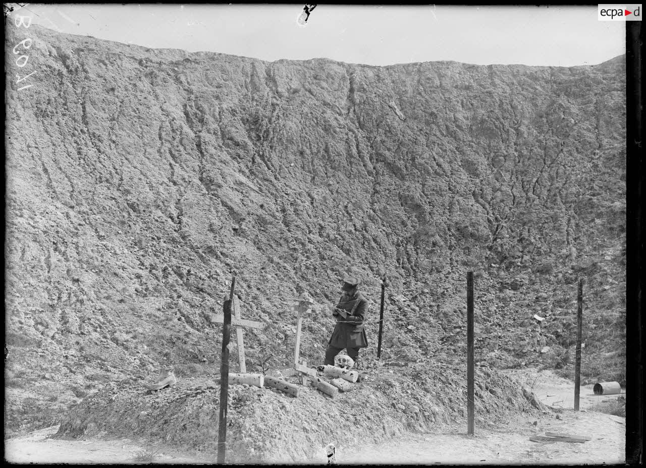 Black and white photo of a man standing in the interior of an enormous mine crater by a burial mound with crosses bones and shell cases. 
https://imagesdefense.gouv.fr/fr/la-boisselle-somme-entonnoir-de-mine-anglaise-28-m-de-profondeur-diametre-60-et-tombes-anglaises-recouvertes-d-ossements-legende-d-origine.html