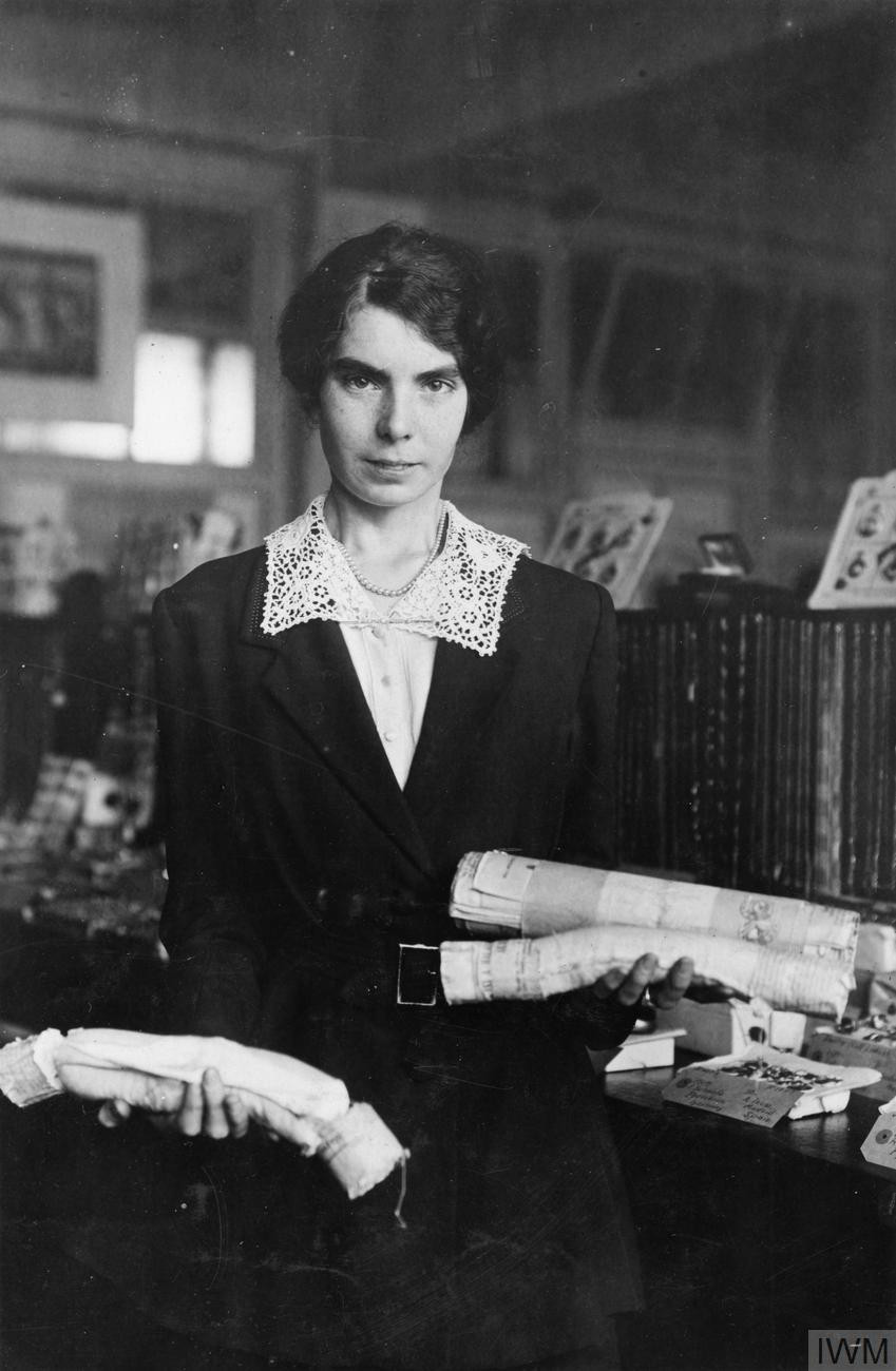 Black & white photo young woman holding three cylindrical bags, standing in an office.