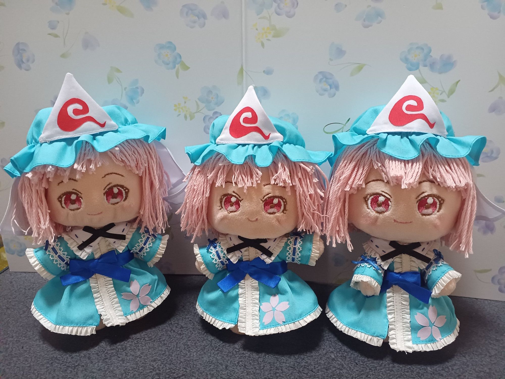 Three plush toys of Yuyuko from the Touhou Project franchise stand in a line against a wall with blue flower designs.