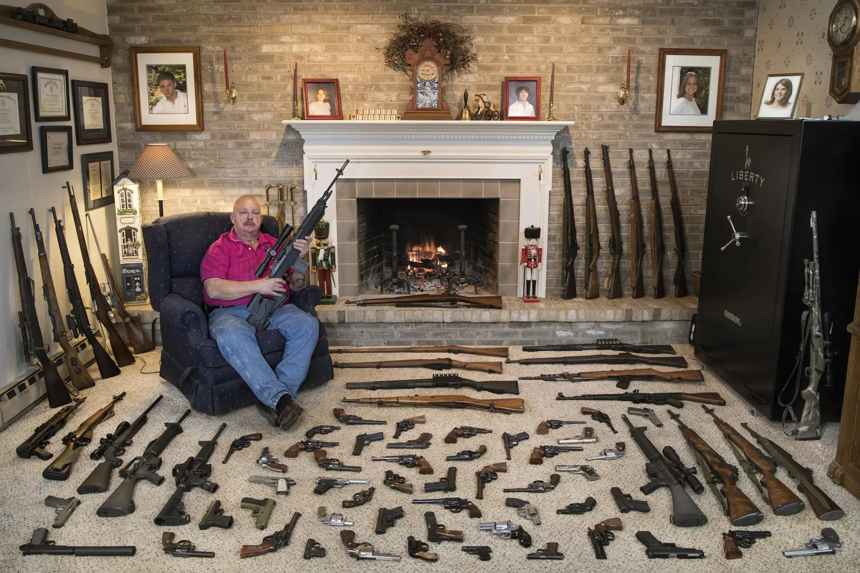 A man in his living room. His living room is full of guns. There's also a big safe labeled "Liberty."
