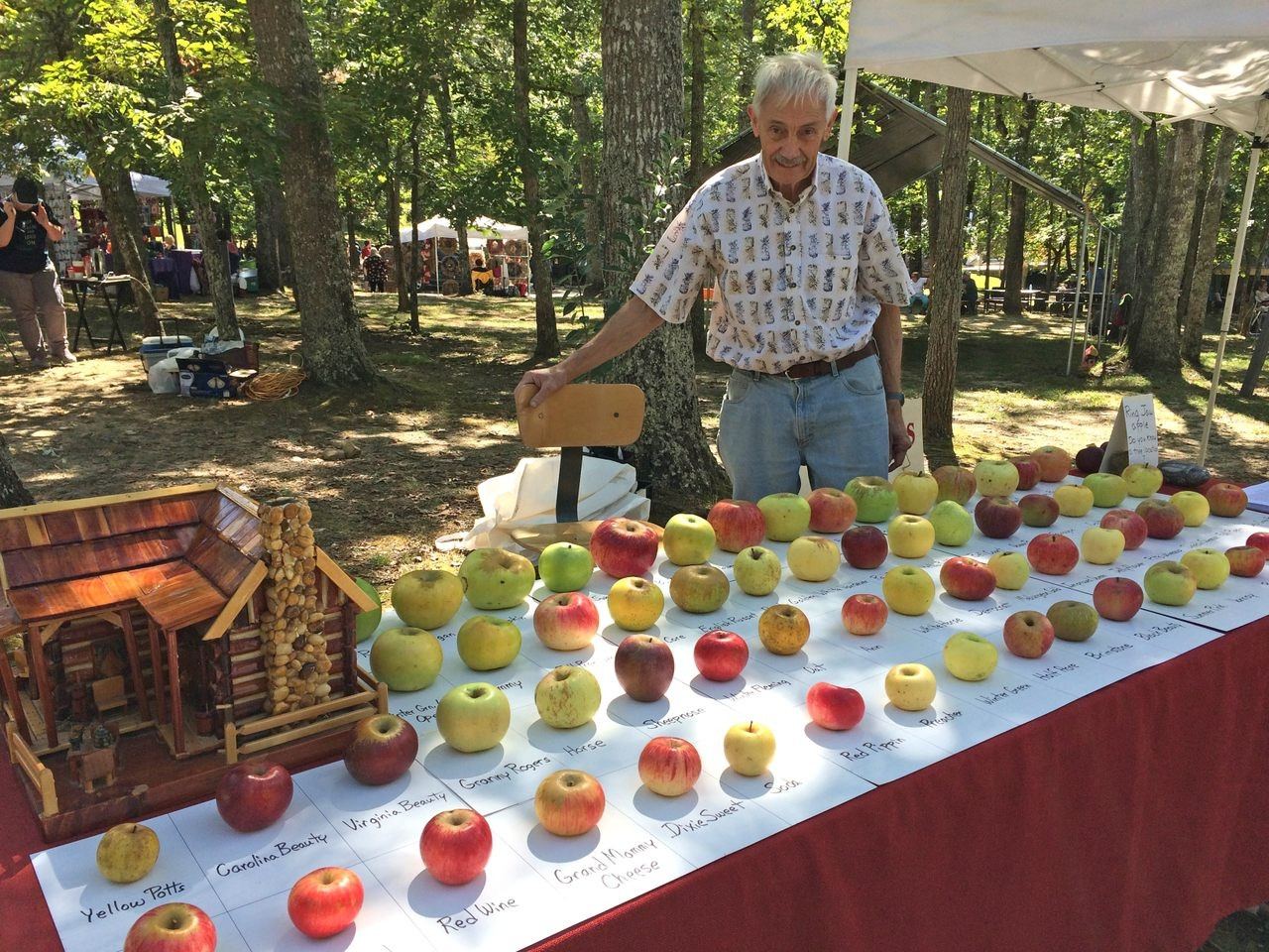 A man behind a table full of apples. 