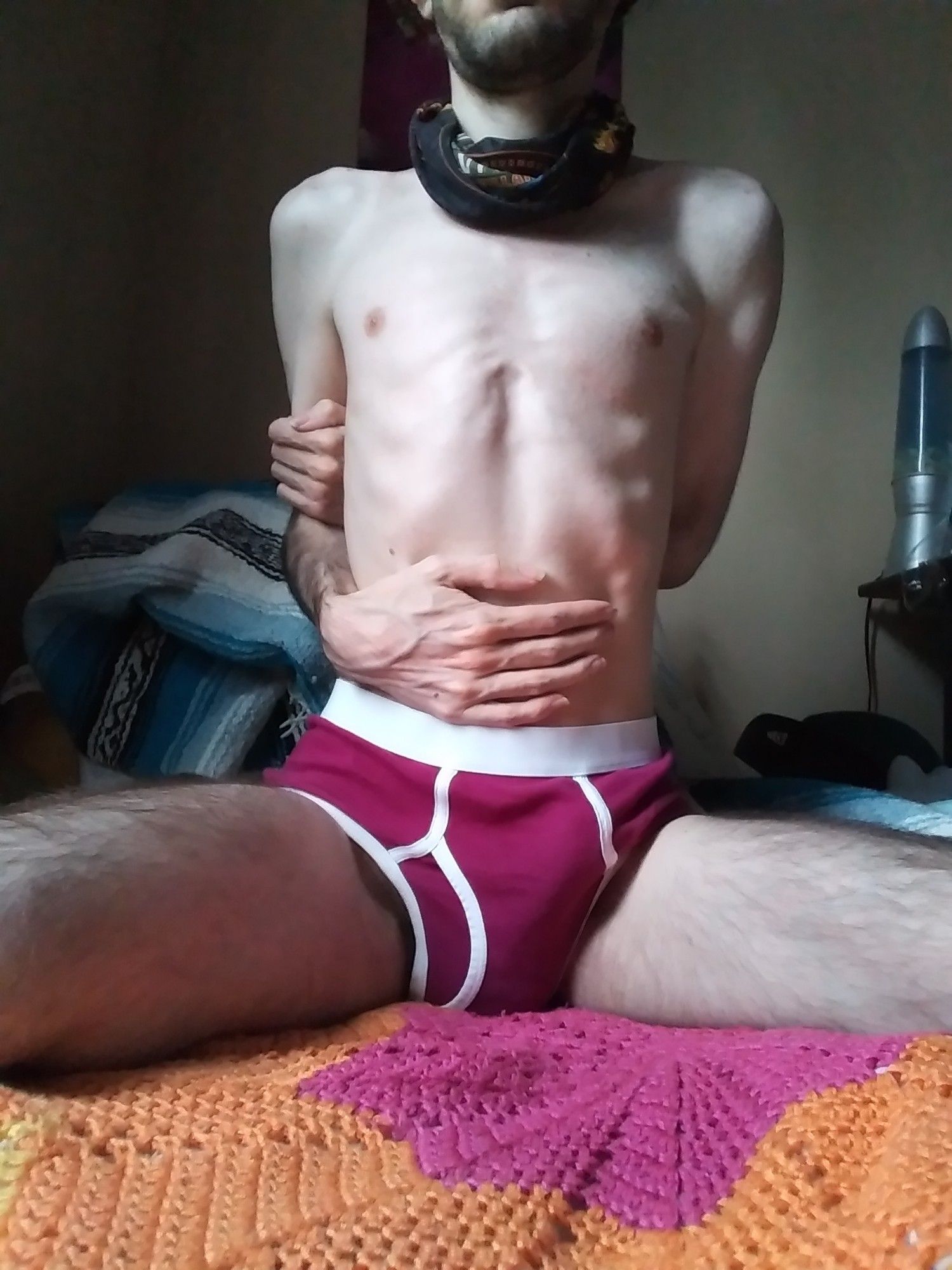 man sitting with his face out of frame, wearing burgundy briefs and nothing else