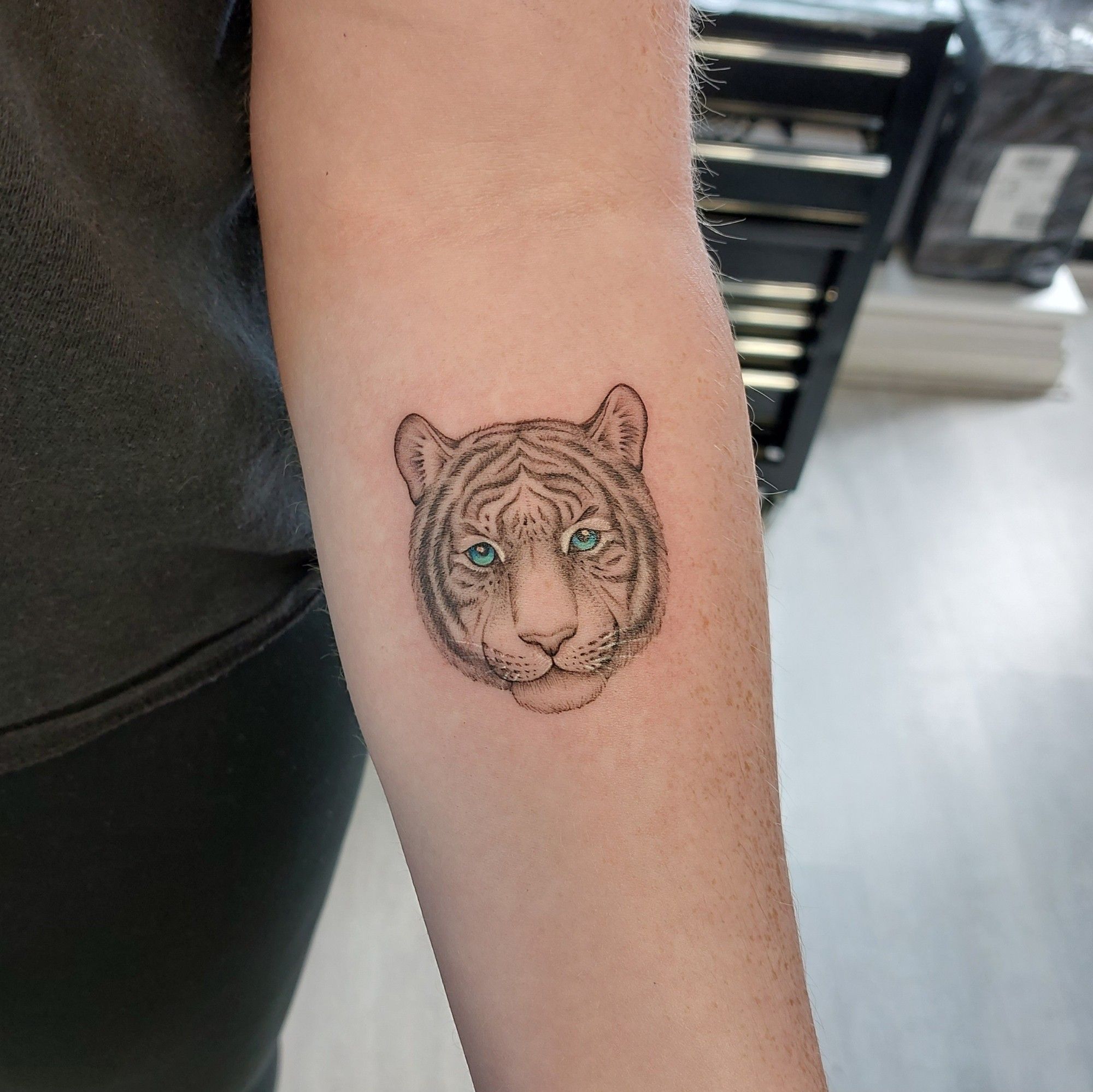 A small, fineline, tiger portrait tattoo on the forearm.