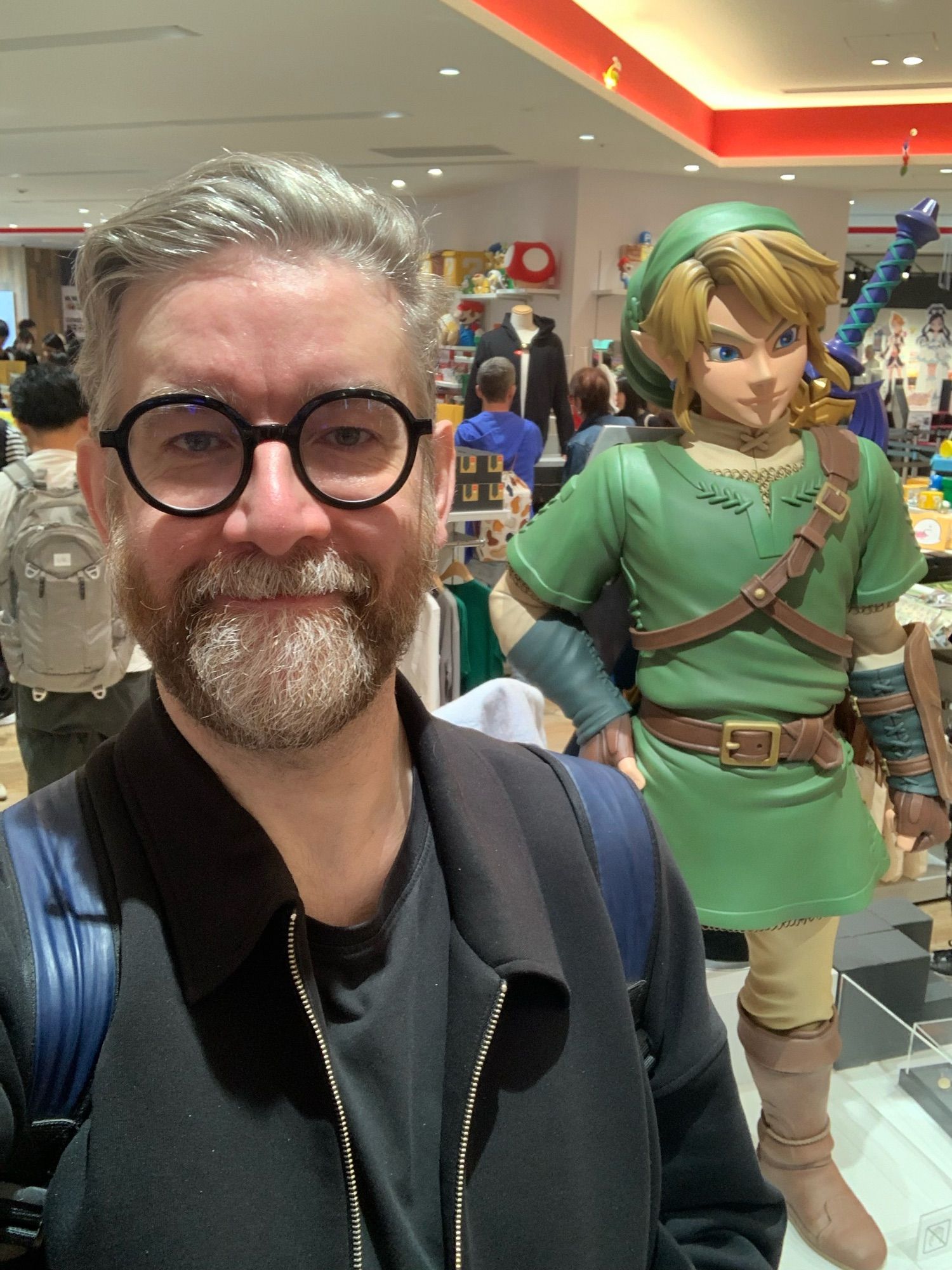 Job-seeking English person in glasses proudly posing next to Link in the Nintendo store.