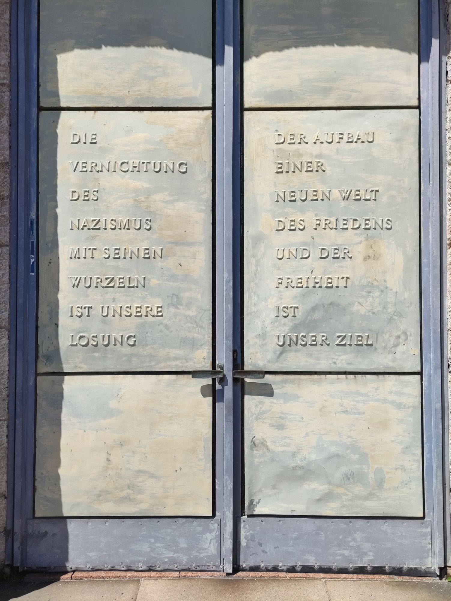 Mahnung auf den Türen des Glockenturms in der Gedenkstätte Buchenwald.
"Die Vernichtung des Nazismus mit seinen Wurzeln ist unsere Losung. Der Aufbau einer neuen Welt des Friedens und der Freiheit ist unser Ziel."