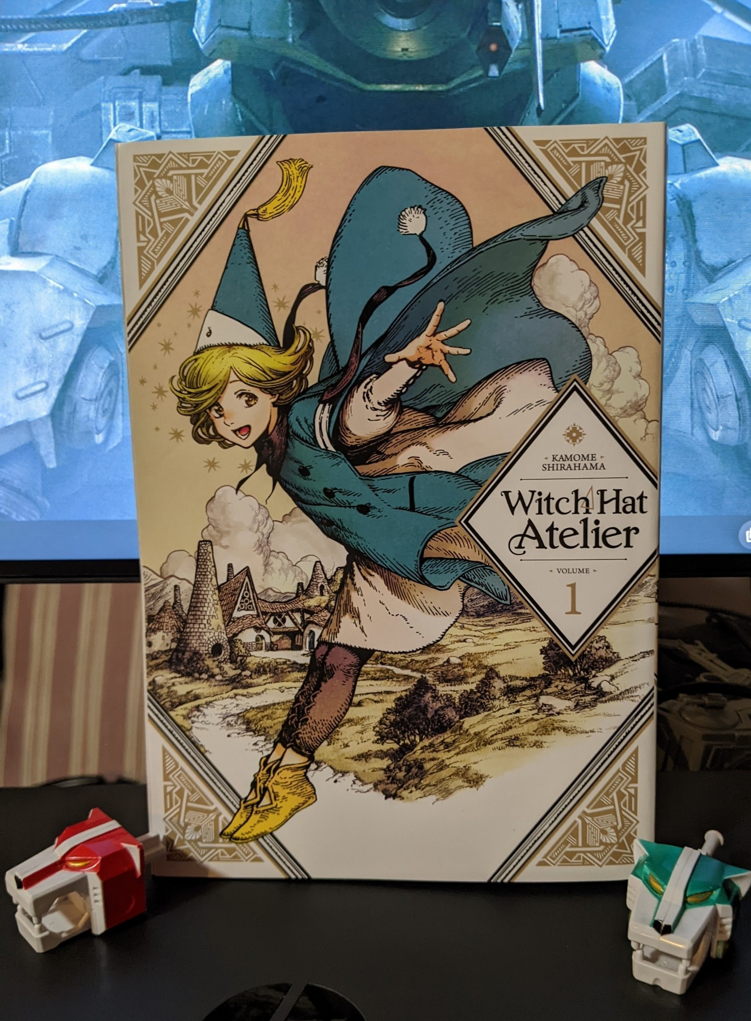 The cover of volume one of Witch Hat Atelier. Also the heads of the Green Lion and Red Lion from the original Voltron arranged tastefully beside the manga.