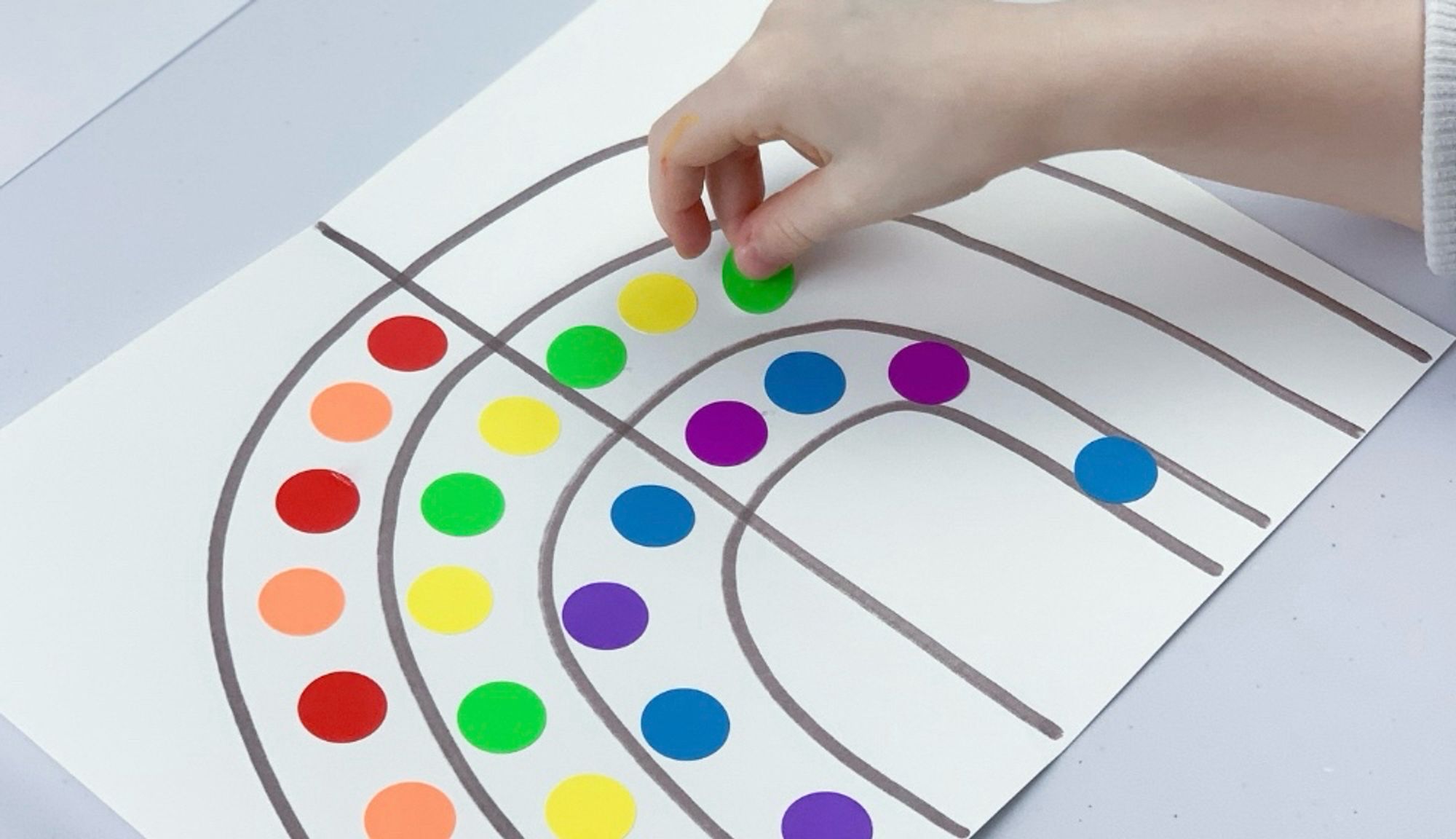 Picture of a hand putting down colorful stickers on a piece of paper where a rainbow was drawn