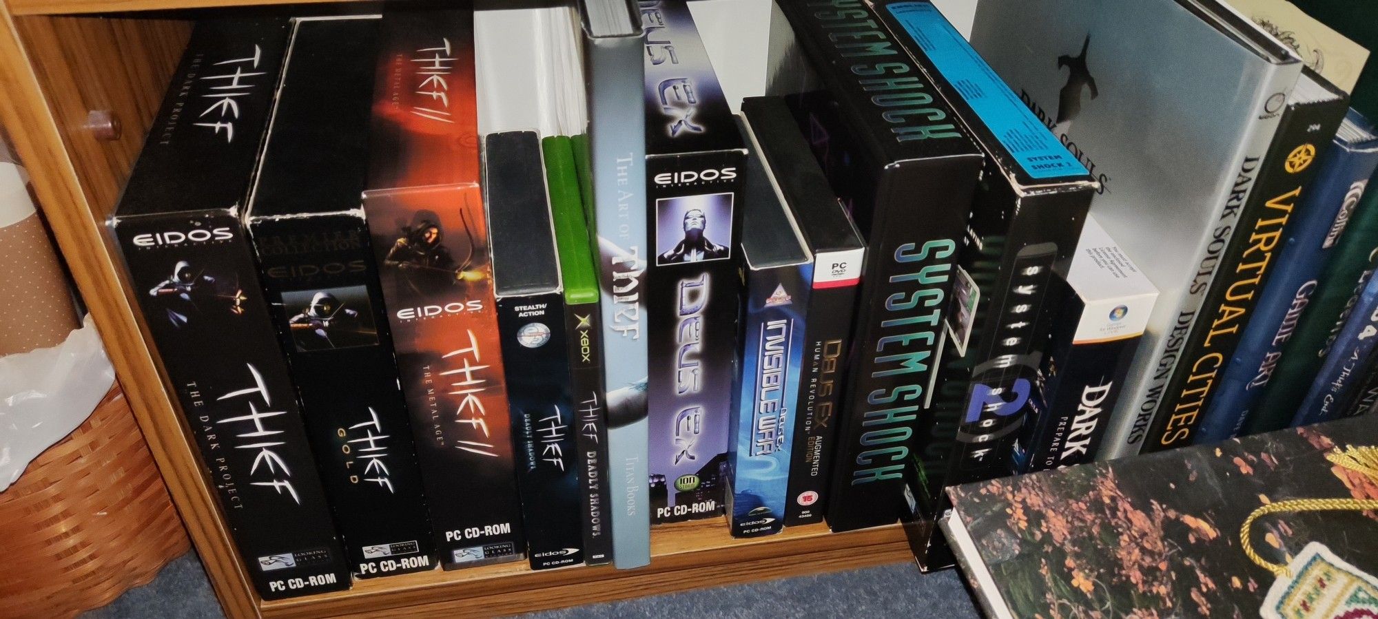 A picture of various PC game boxes on a wooden shelf.
The game boxes are of various sizes, with some being large 'big box' PC games.