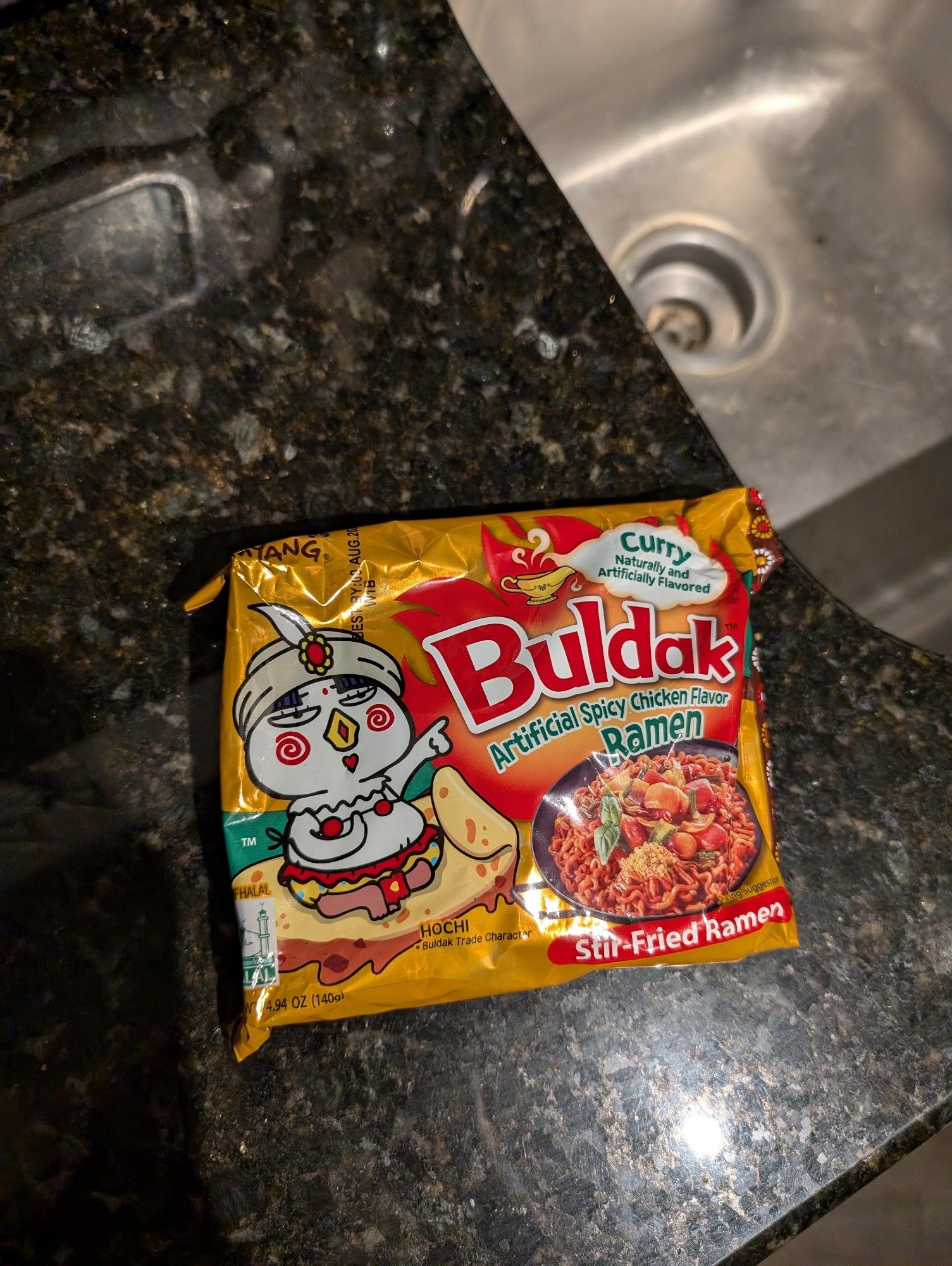 A packet of Buldak curry ramen. Yellow plastic with a cartoon chicken wearing a bikini and a turban.