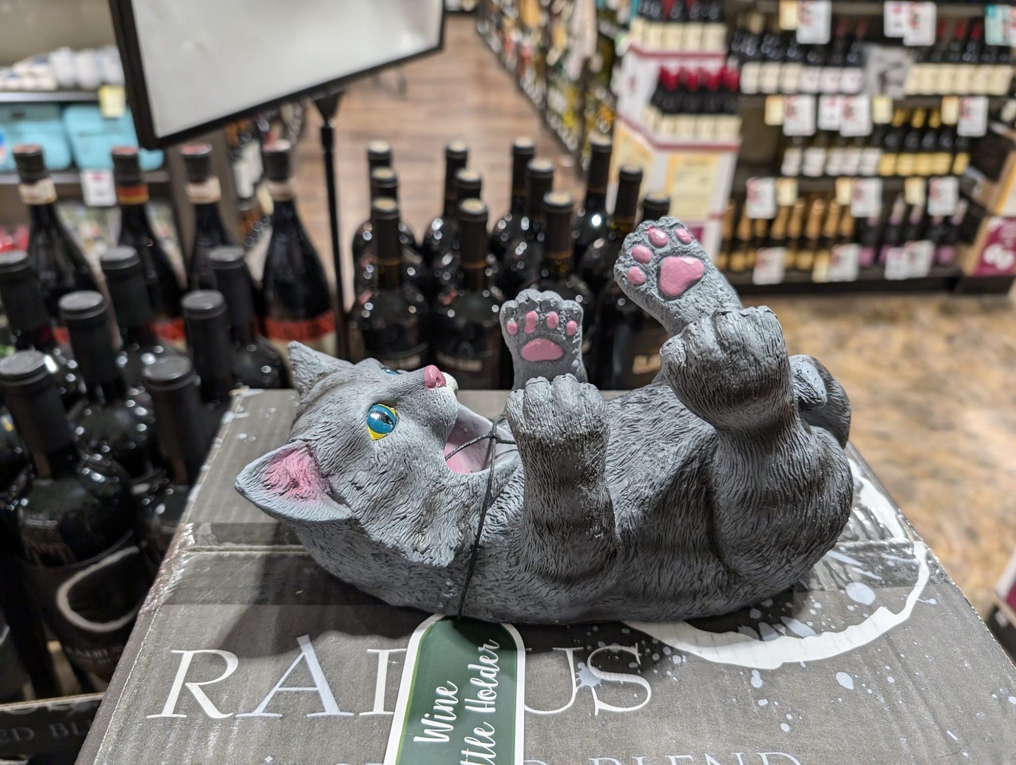 A grey plastic cat on its back with its mouth open and its arms outstretched where you can store a bottle of wine.