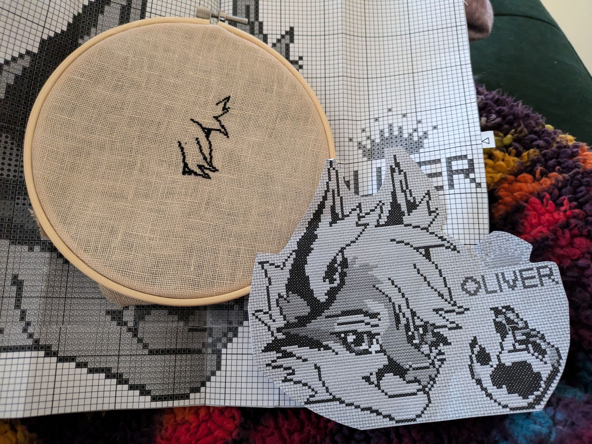 Midway of da one cross stitch progress. Including a slightly enlarged preview of what the final piece will be. Headshot of lynx 3/4 view with floating hand in a relaxed wave and a crown over the name "Oliver"