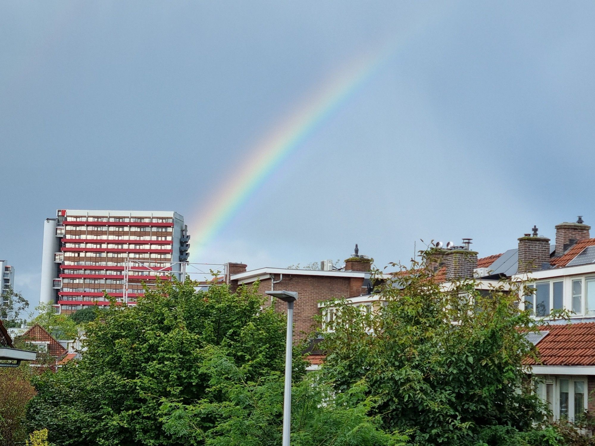 Foto van de lucht met regenboog die precies eindigt in de rode flat aan de van Lieflandlaan