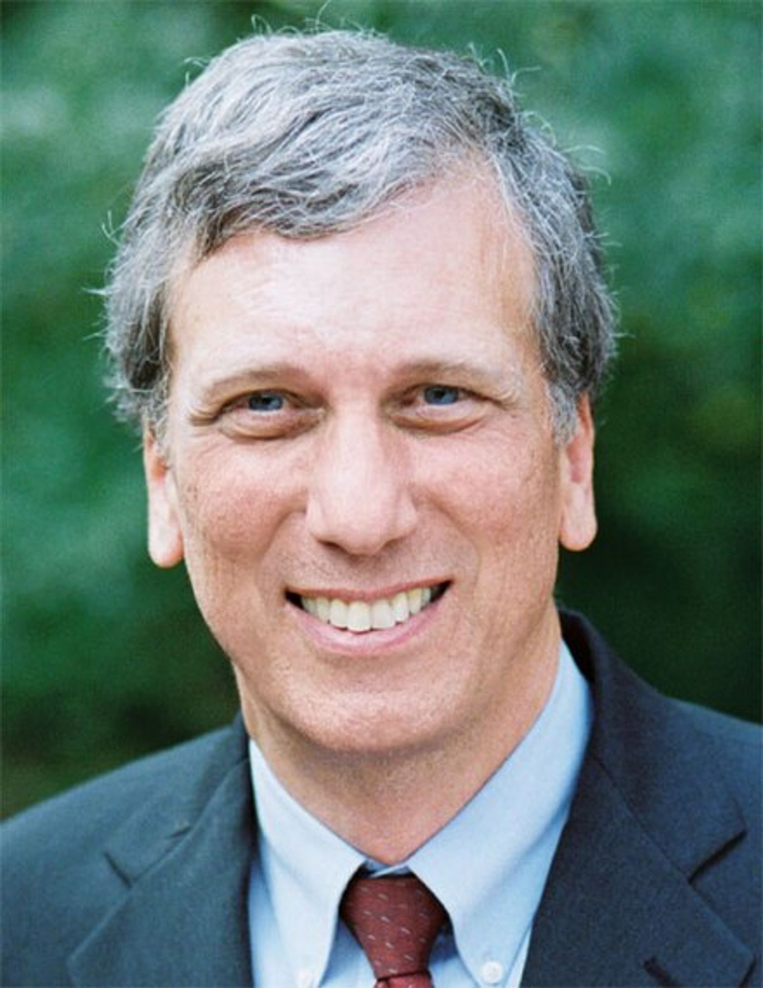 Eisen headshot photo. Smiling middle-aged man with grey hair, wearing collar, suit, and tie.