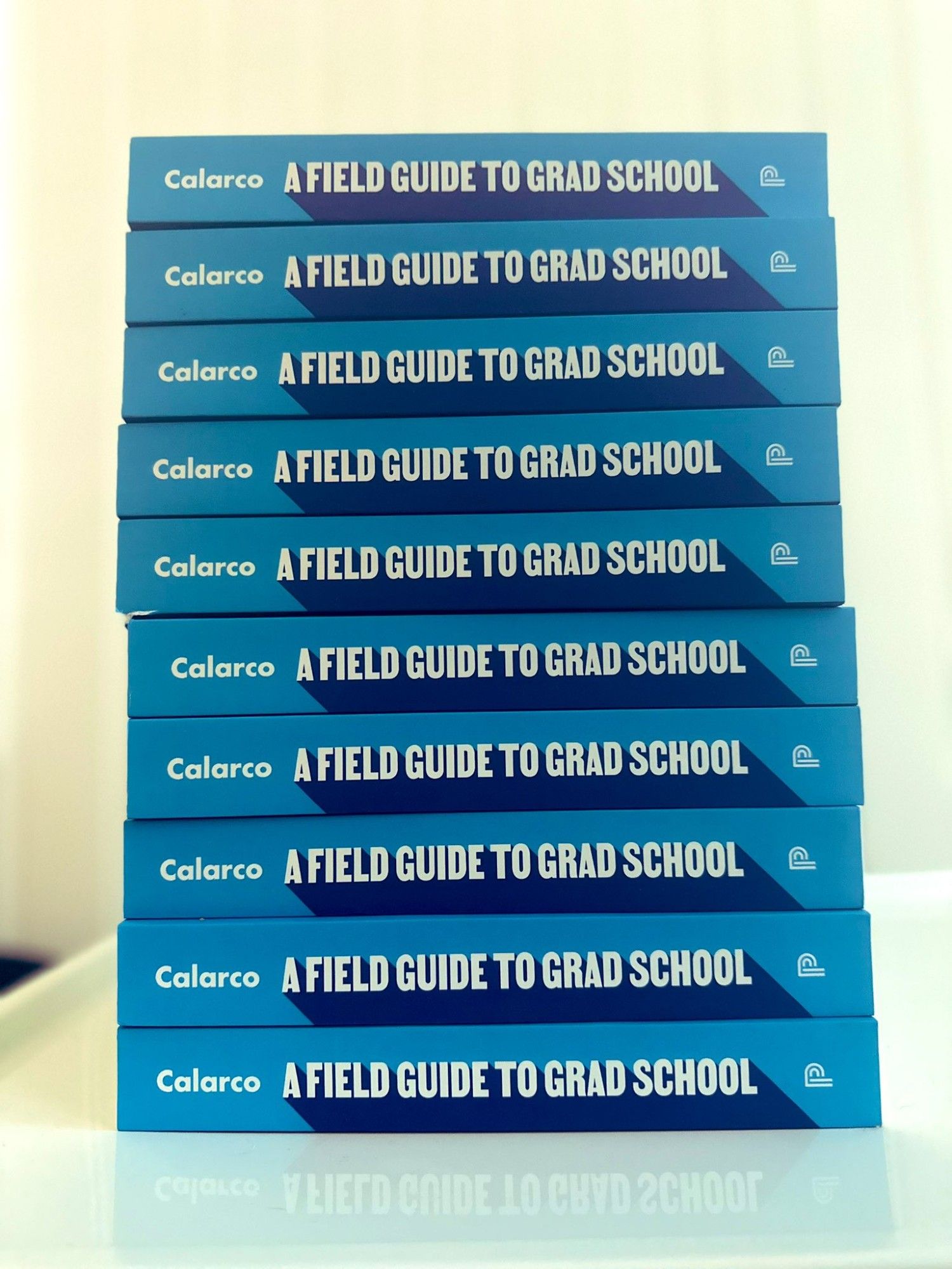 A stack of 10 copies of A Field Guide to Grad School with the book spine showing.