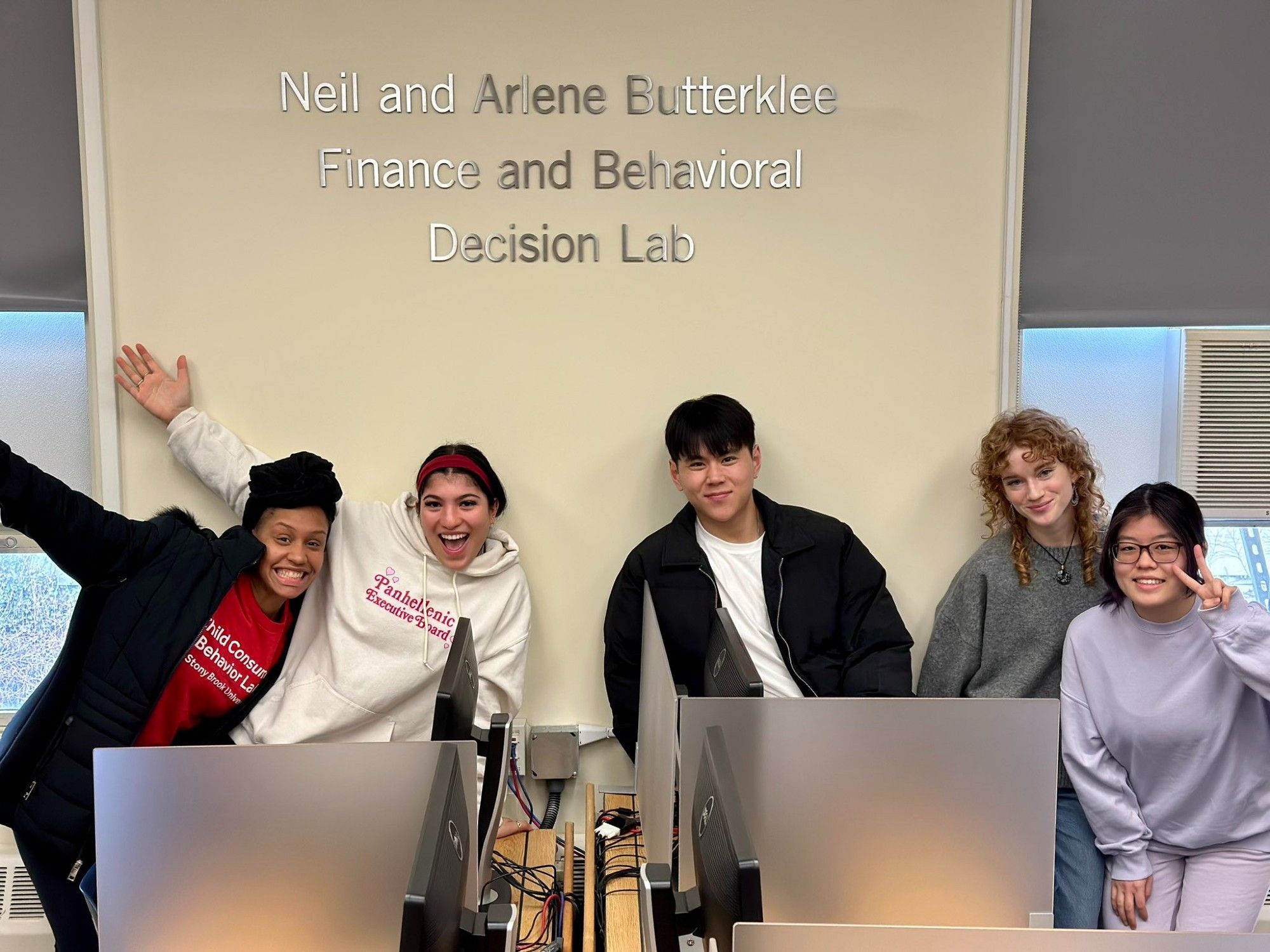 Group shot of 5 students under a sign that reads “Neil and Arlene Butterklee Finance and Behavioral Decision Lab.”