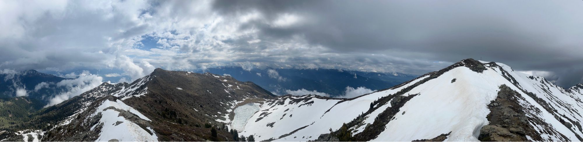 Panoramic view of the Italian alps, peaks are still partially snow-covered. Cloudy sky