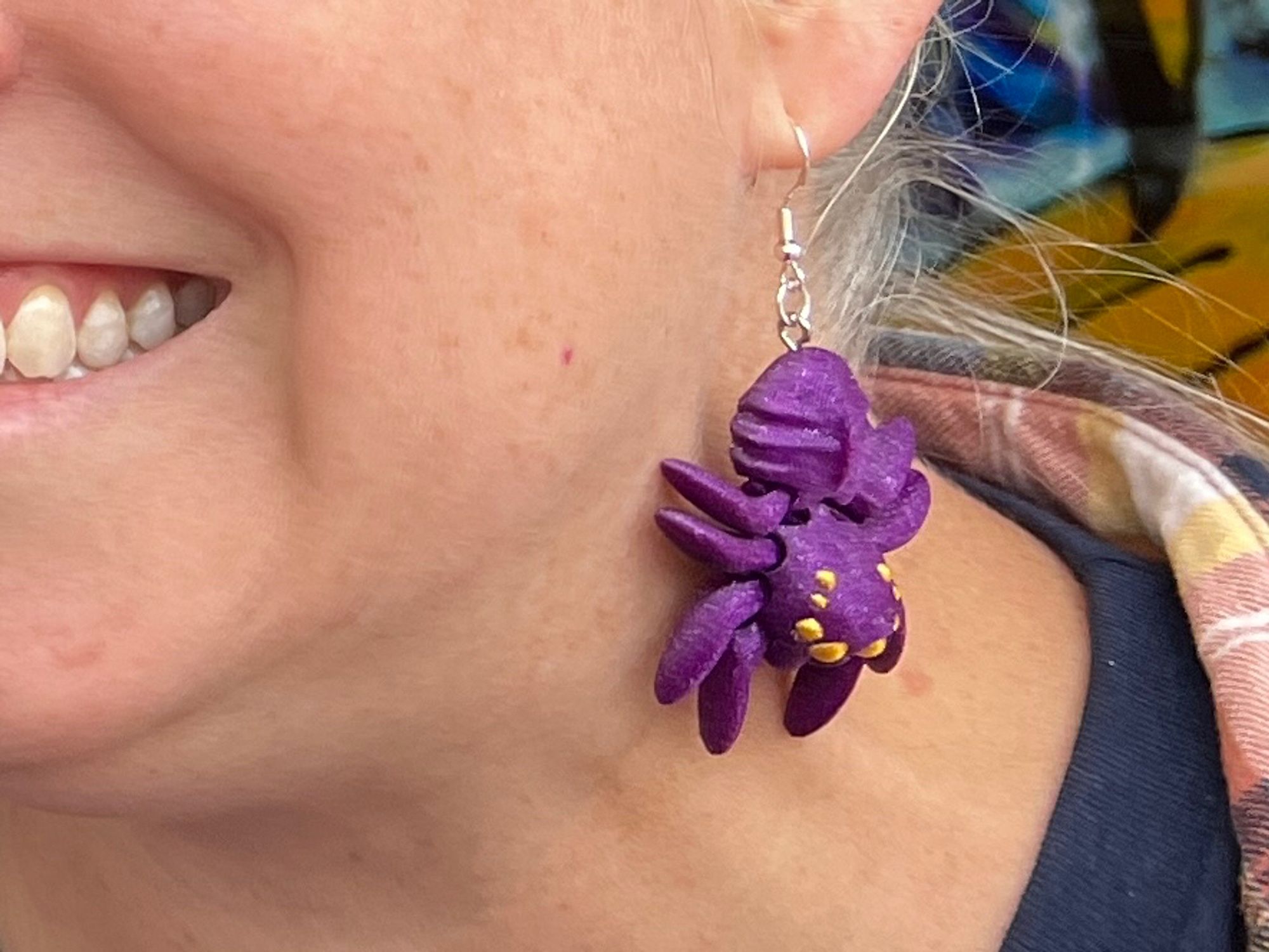 Purple spider earring with gold eyes dangling from an ear