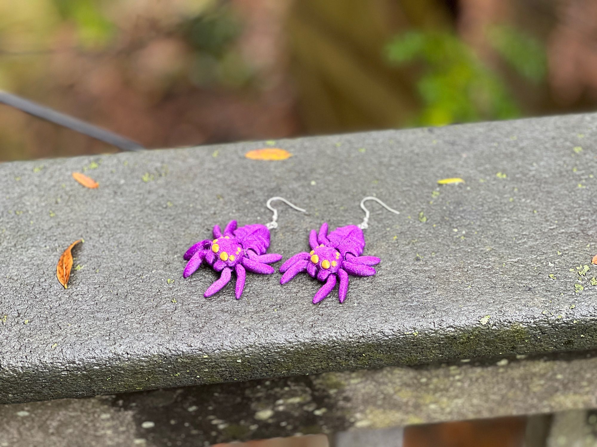 Purple spider earrings with gold eyes on a gray railing outside