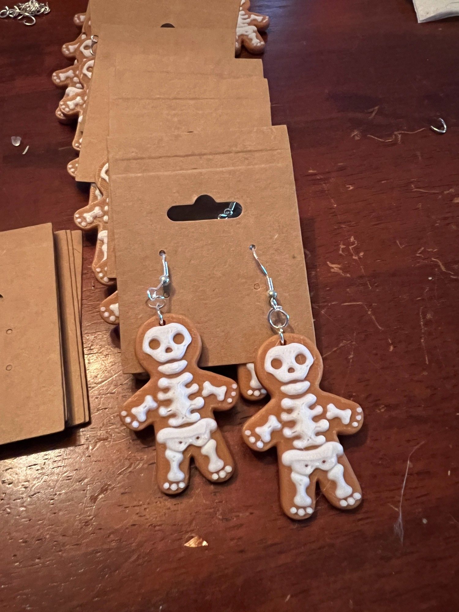 gingerbread skeleton cookie earrings, 3d printed in a light brown with white "frosting" that depicts a skeleton on top of a person shaped cookie