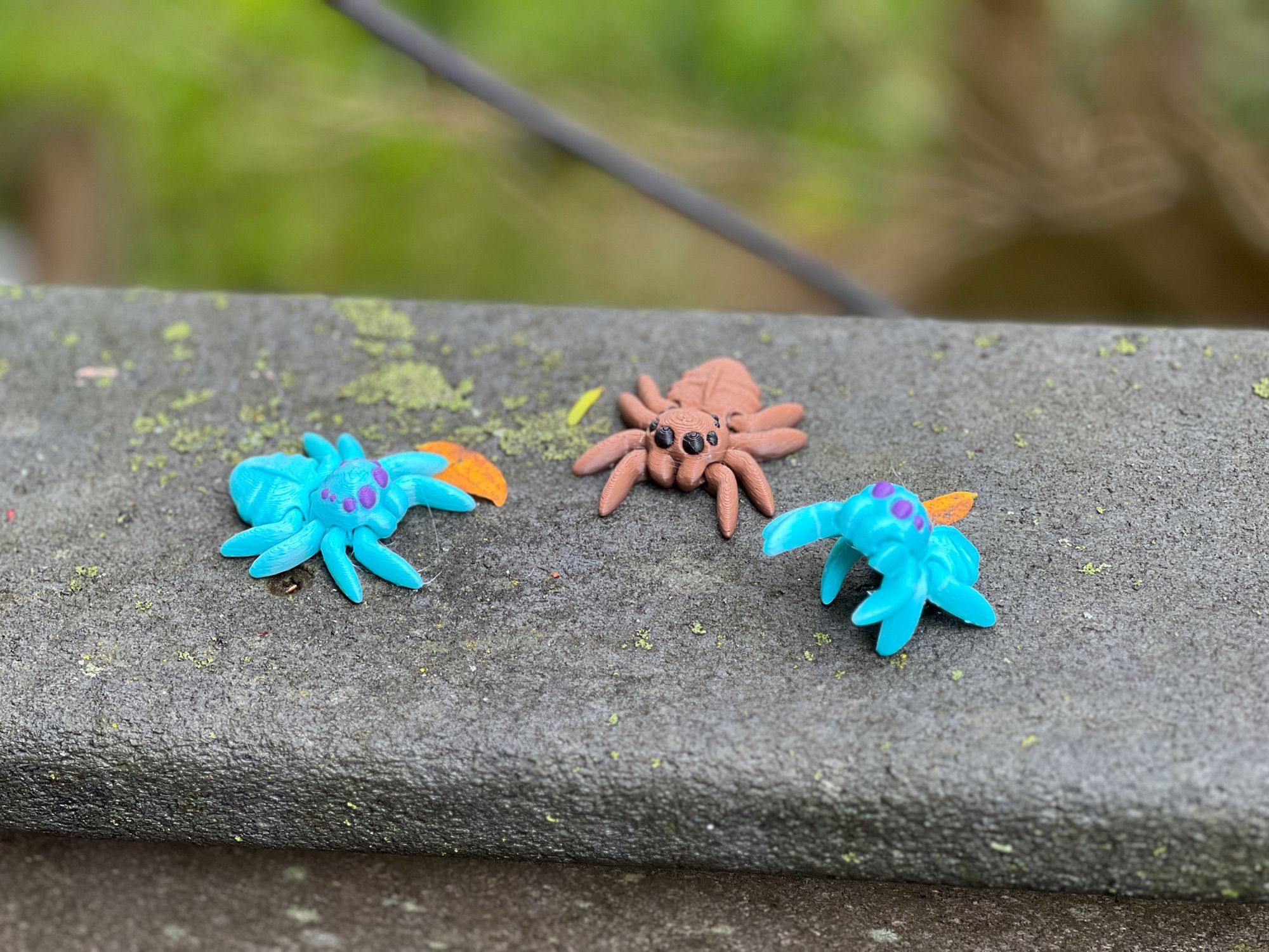 Three spiders, two in teal with purple eyes, one brown with black eyes. One of the teal spiders is standing