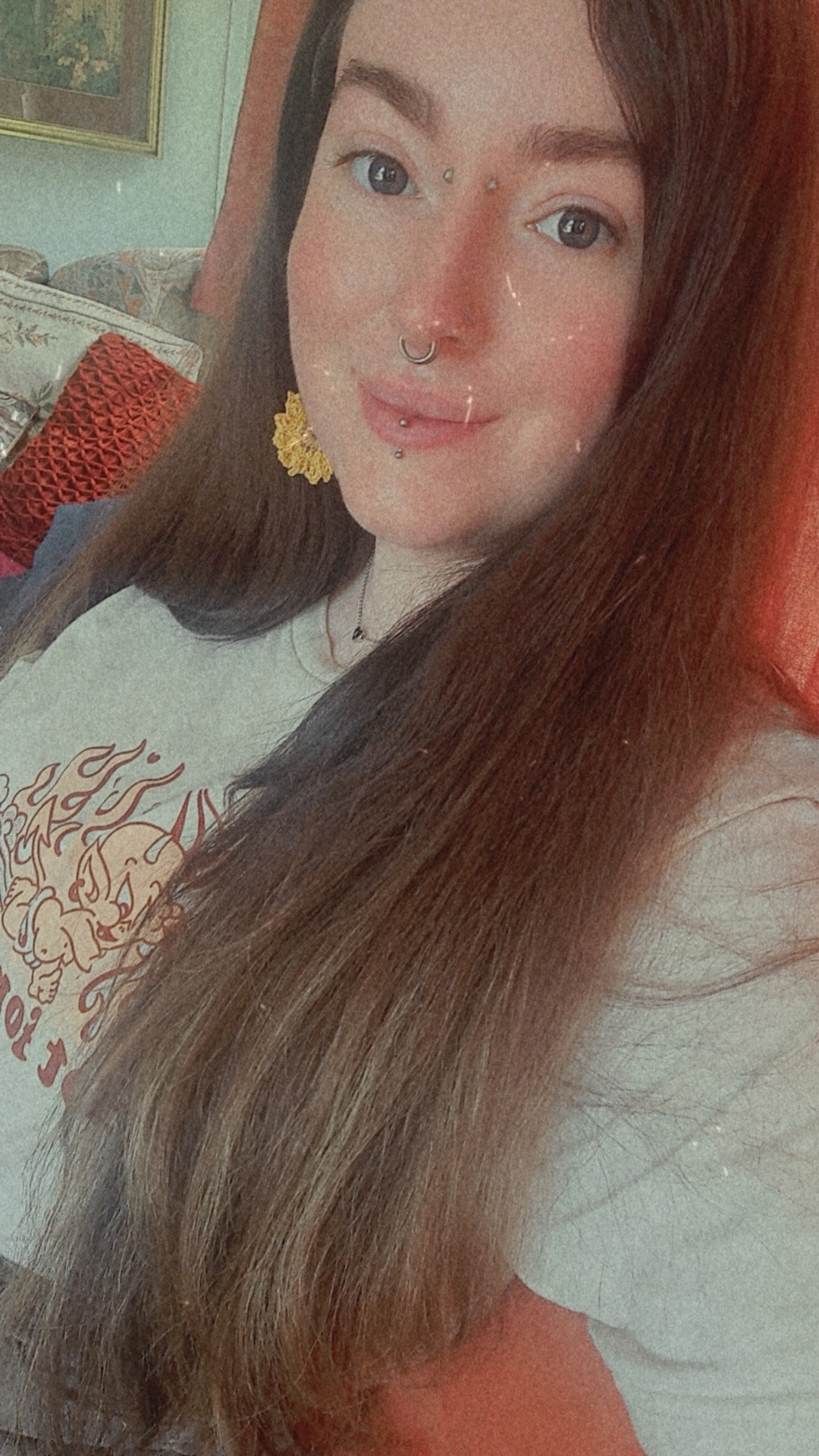 Snapchat selfie (28yo white woman with long brown hair and facial piercings. Wearing a white retro style devil tshirt and crochet sunflower earrings) 