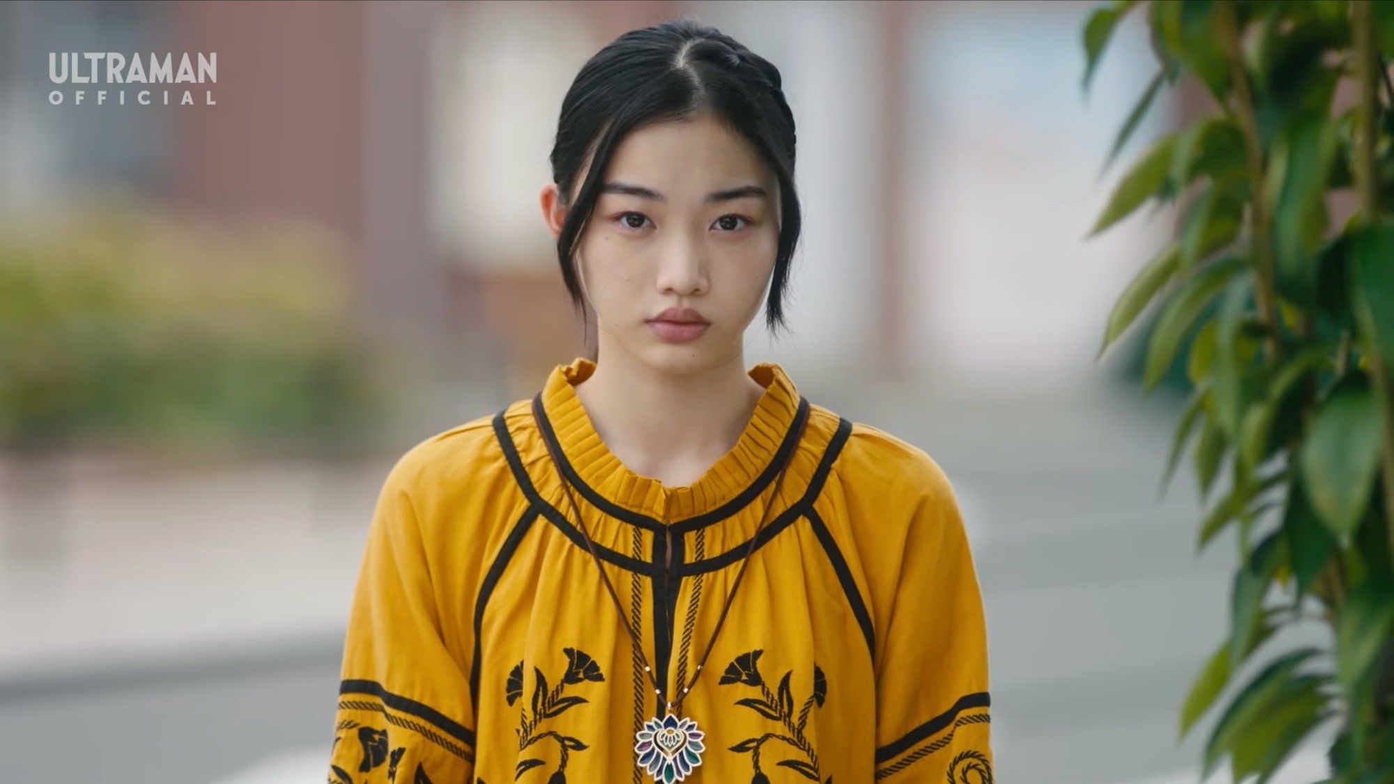 Screencap: A young woman in a yellow dress stares at the camera with a sad expression.