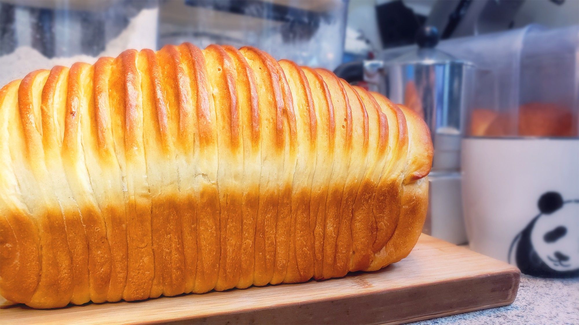 Photo: A loaf of milk bread styled in the "wool bread" cut with parallel narrow strips of dough rolled around it before baking.