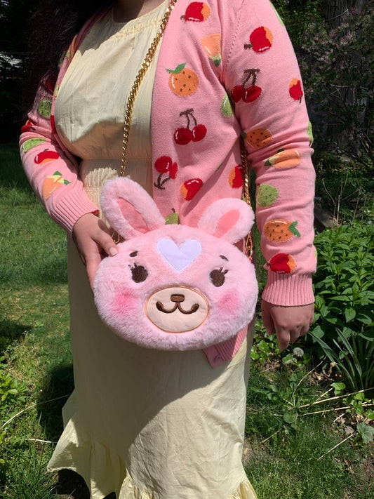 A person with a pink cardigan and yellow dress showing off that they are wearing a pink stylized fluffy bunny purse.