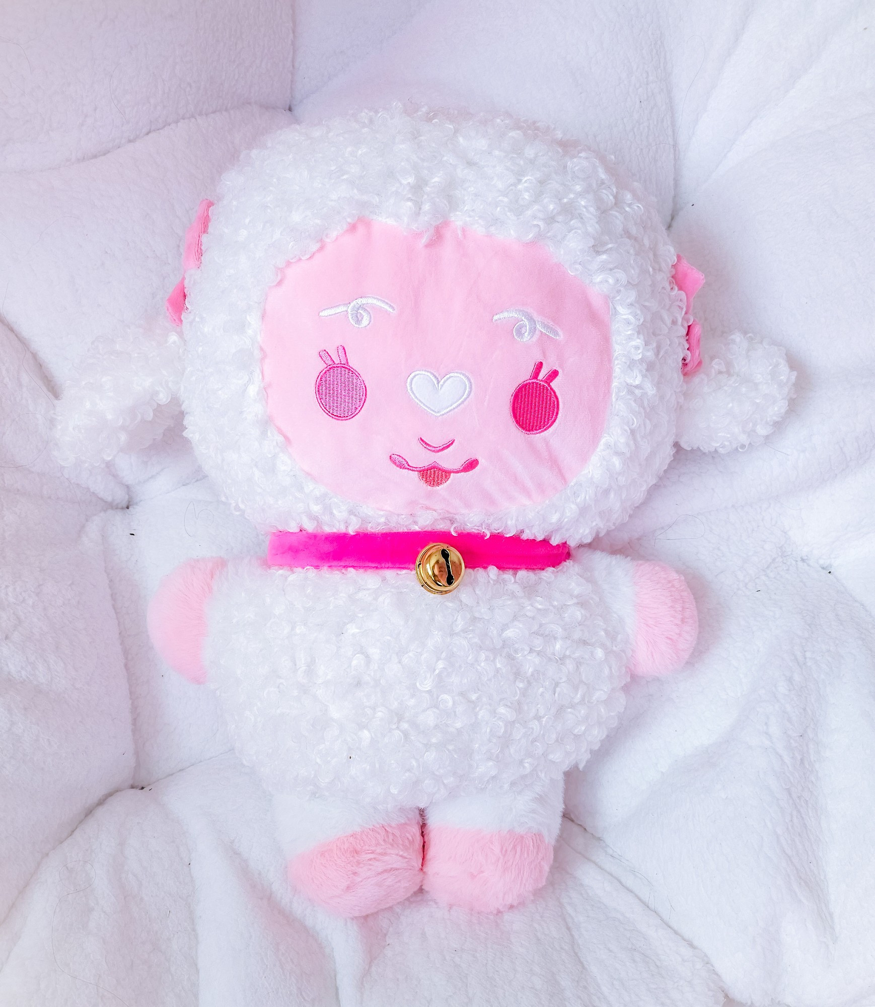 A stylized bipedal large fluffy white sheep plush with a pink face and bows on her ears.