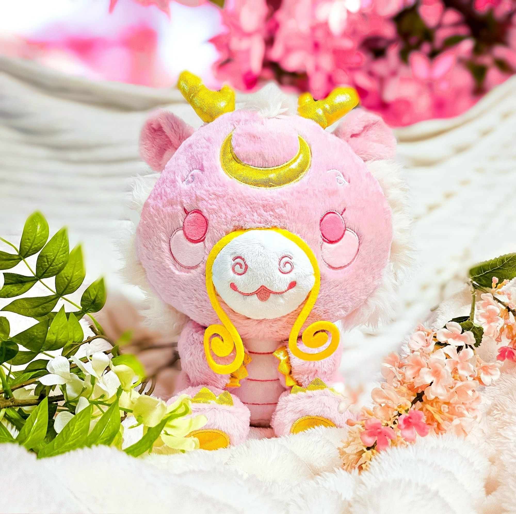 A stylized bipedal pink Chinese-style
dragon plushie with gold accents
surrounded by various flowers