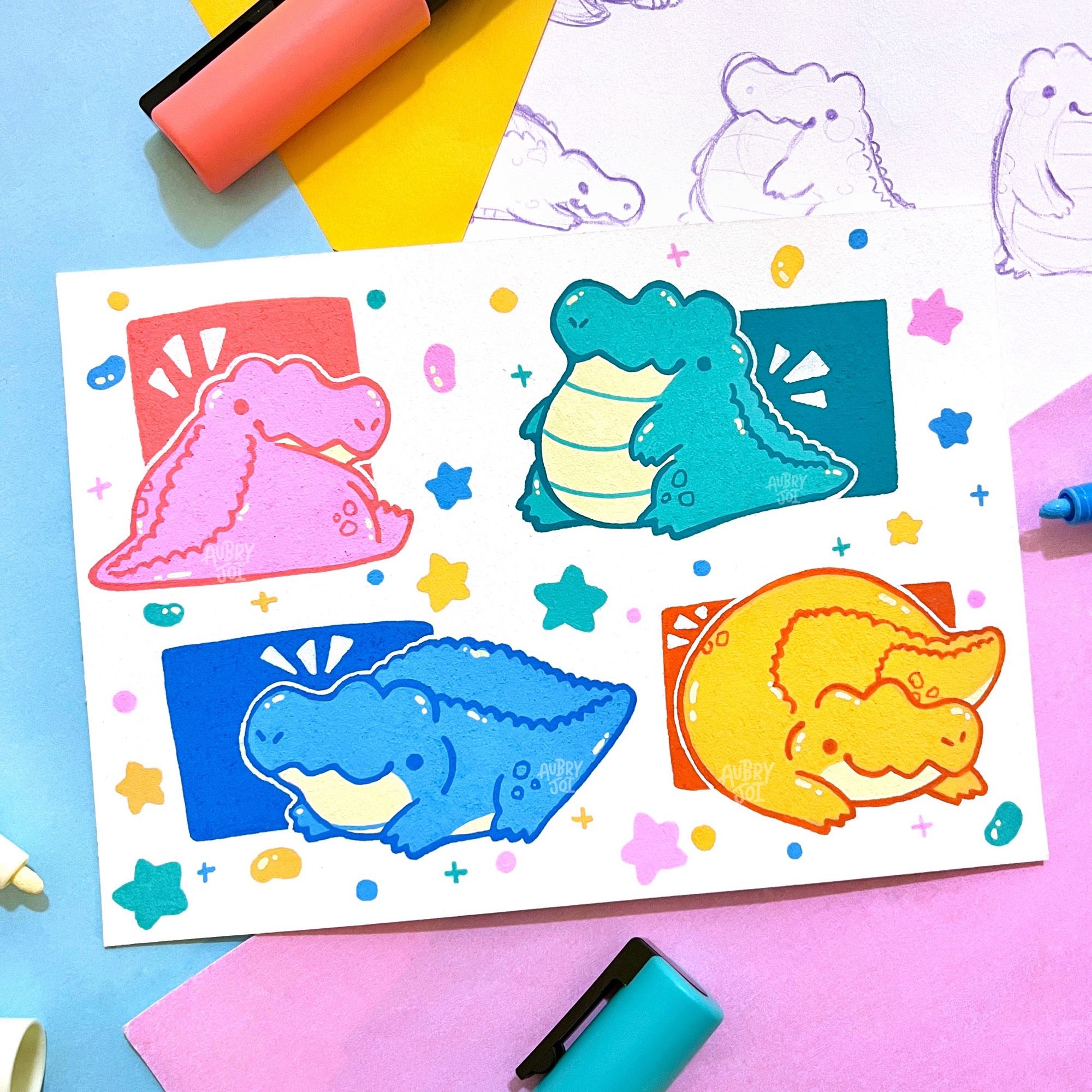 A paint marker illustration of four cute, stylized, stubby alligators on one page. They all have short legs, chubby bodies, no necks, and small dot eyes with goofy smiles. One is pink, one is teal, one is blue, and one is yellow-orange. There are small stars, jellybeans, and sparkles floating around them all.